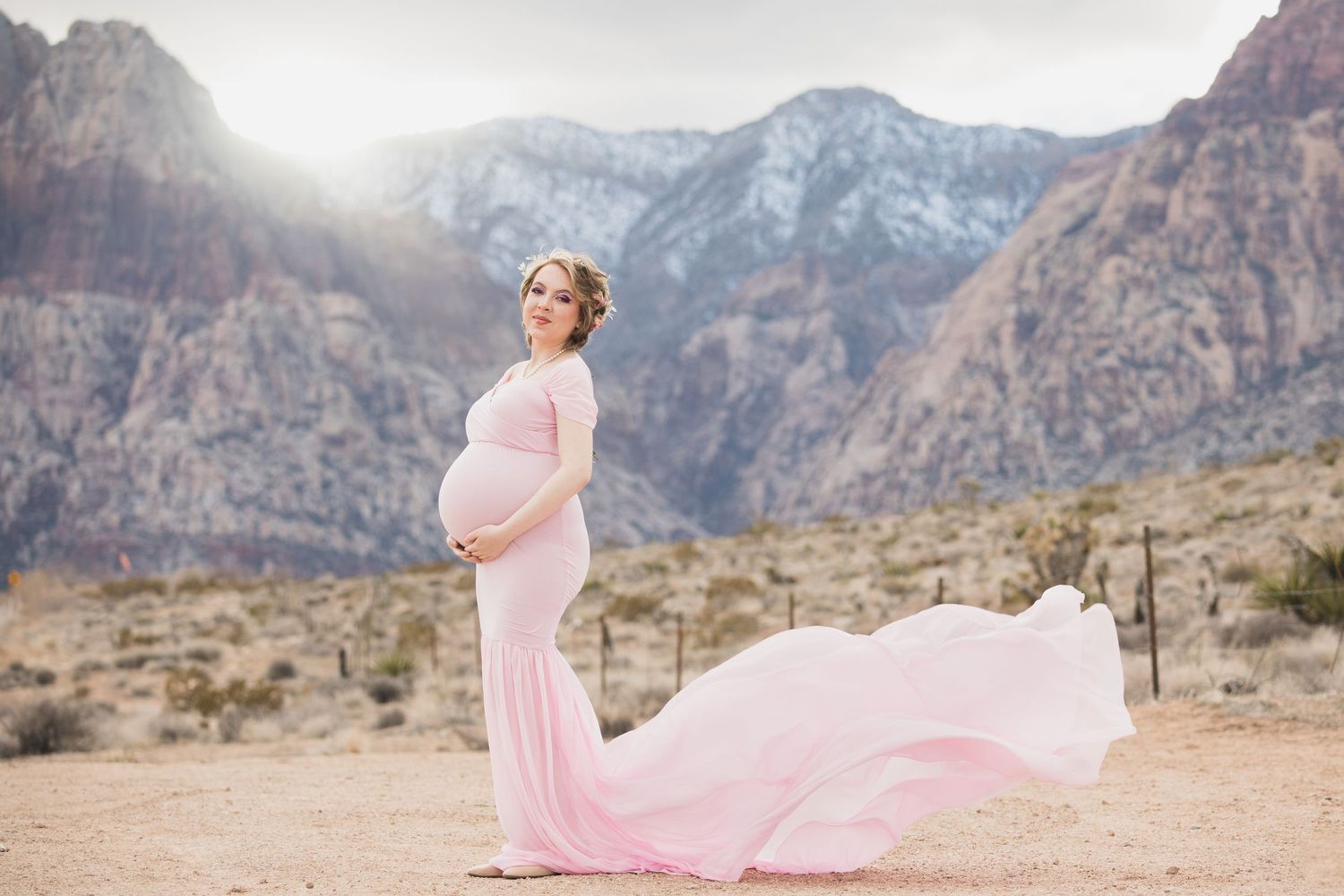 Flowing pink maternity gown catches wind against majestic Red Rock Canyon backdrop.