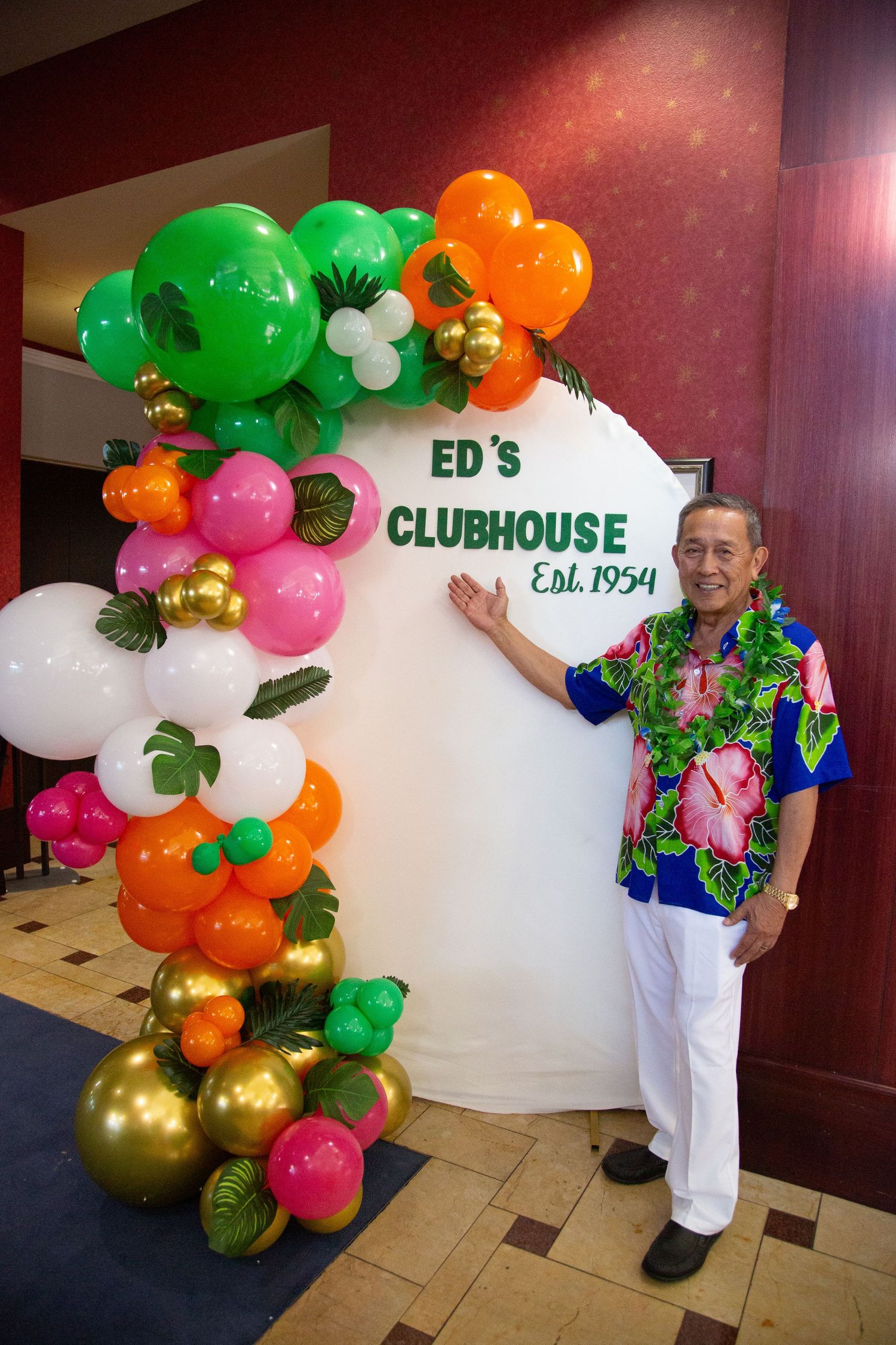 Festive balloon arch with green, orange, and gold decorations frames a clubhouse entrance sign.