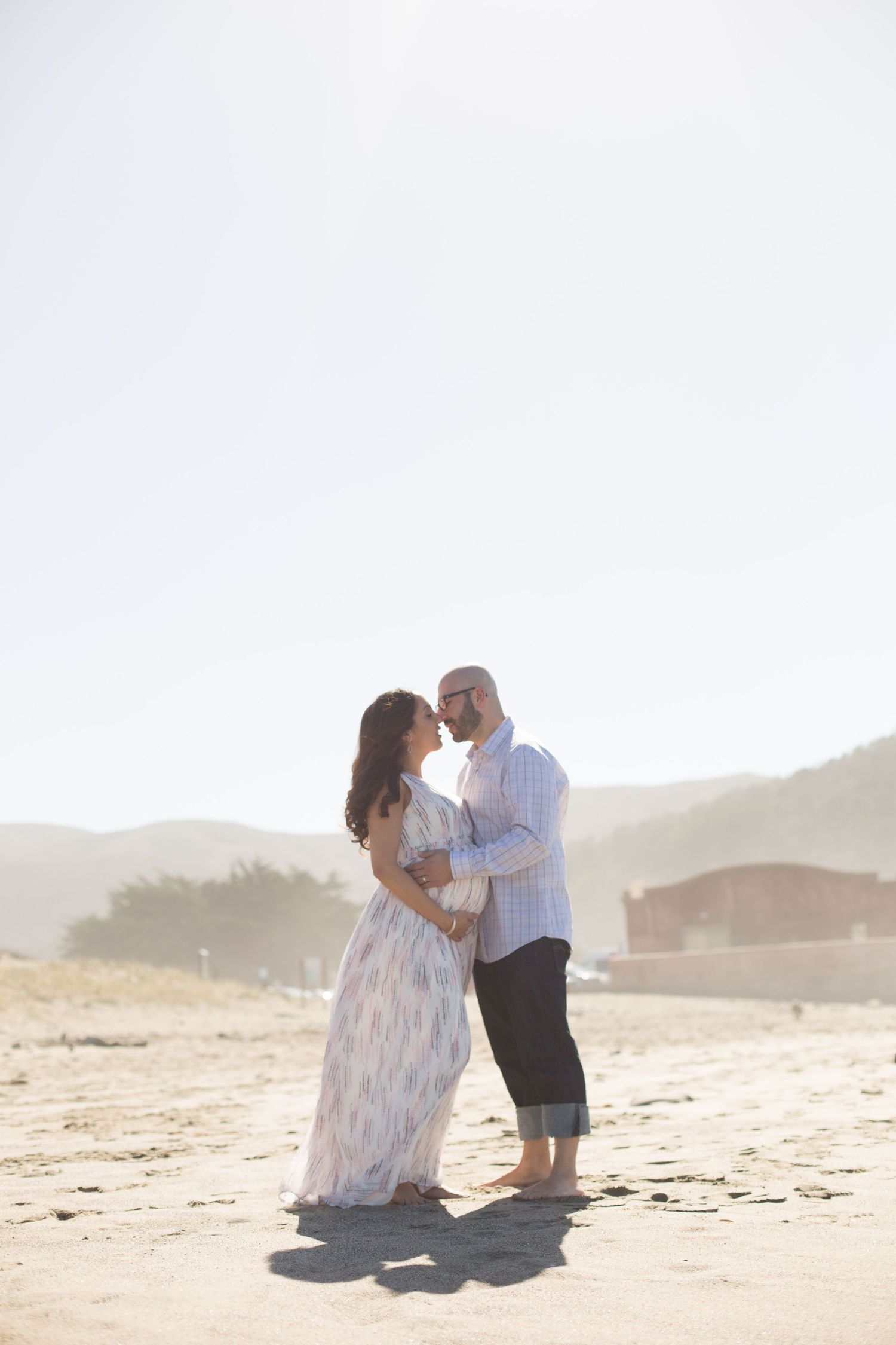Couple shares intimate moment on beach at sunset with mountains in background.