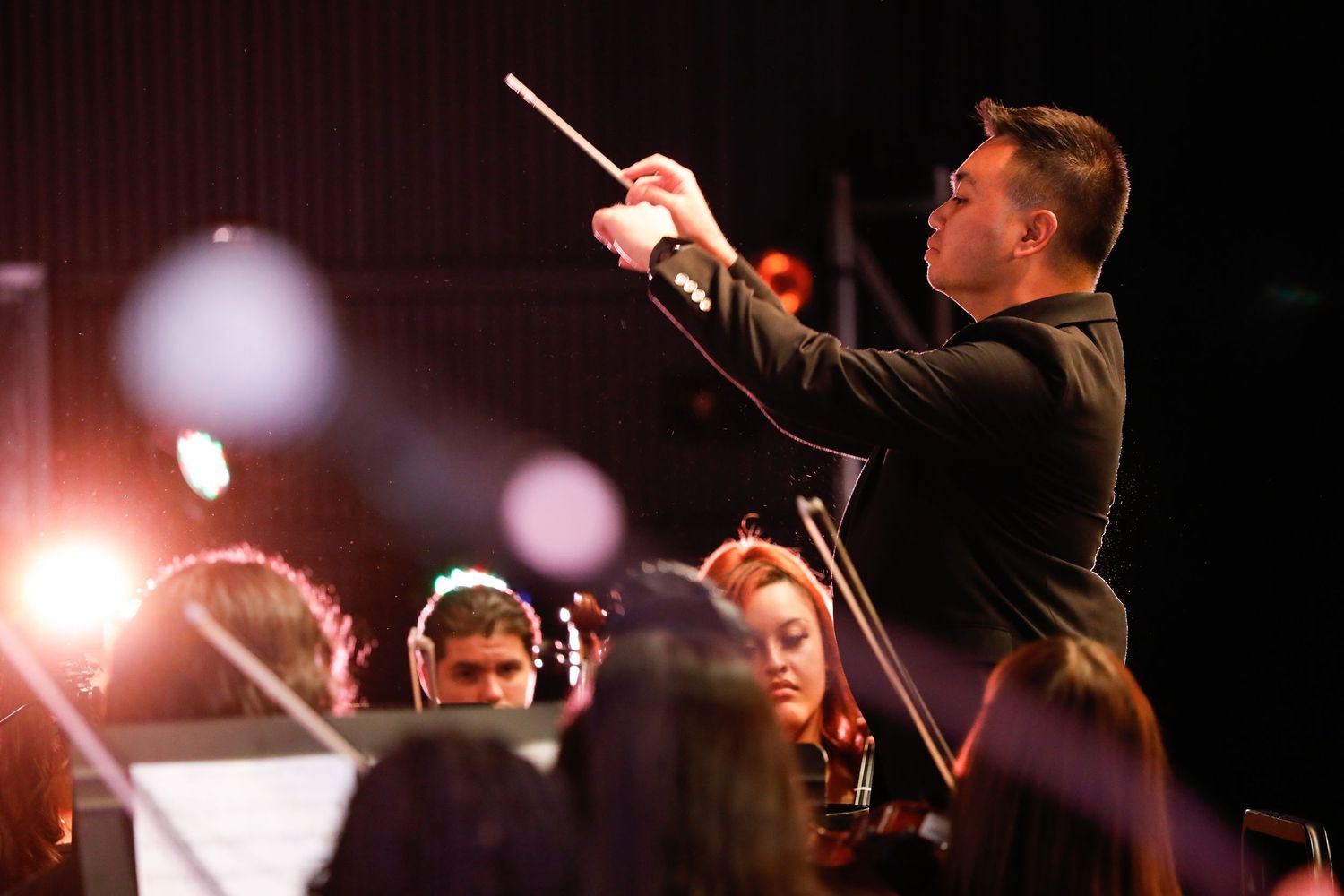 Conductor leads orchestra with baton raised high during dramatic concert performance.