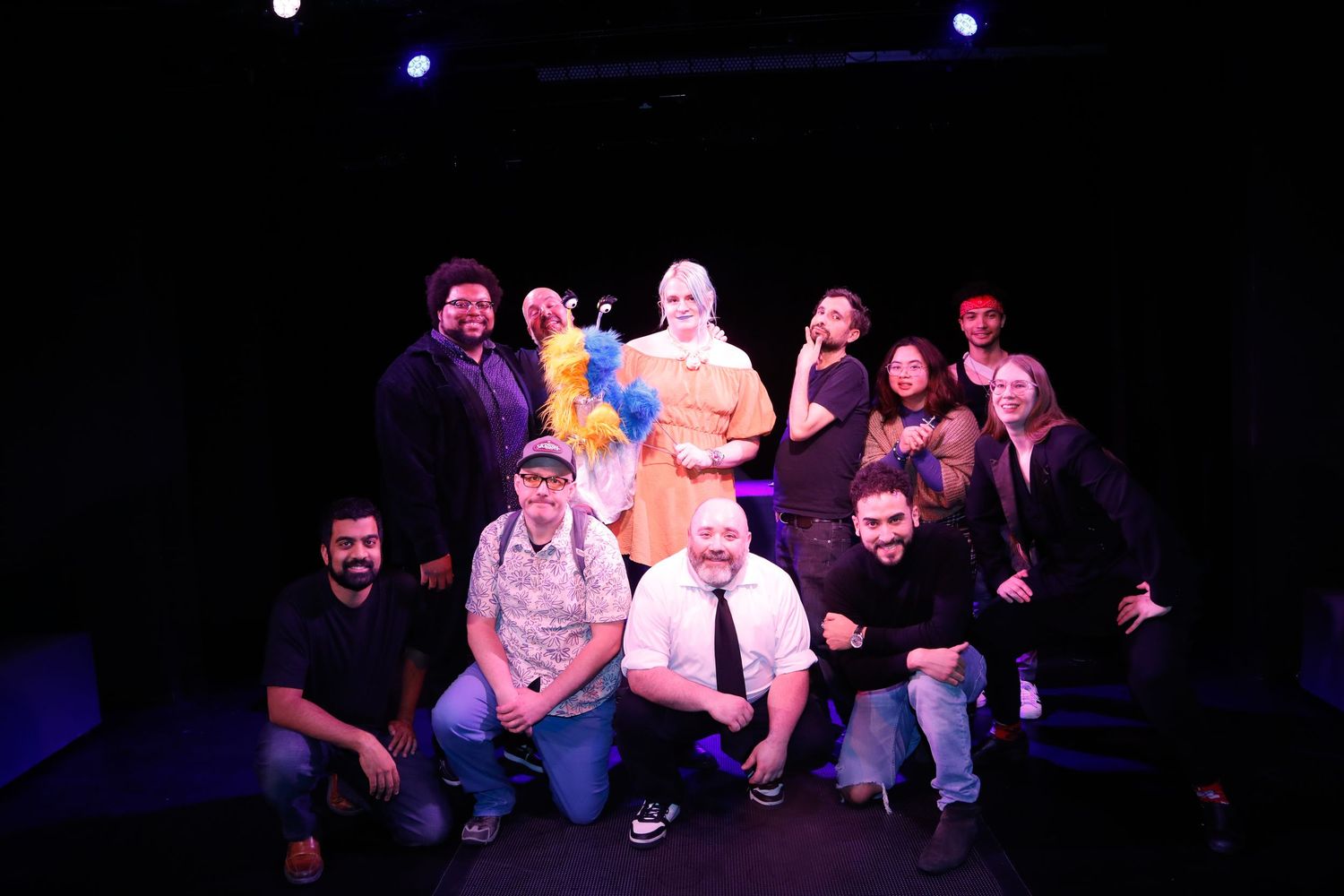 Group of performers sitting on stage under blue theatrical lighting.