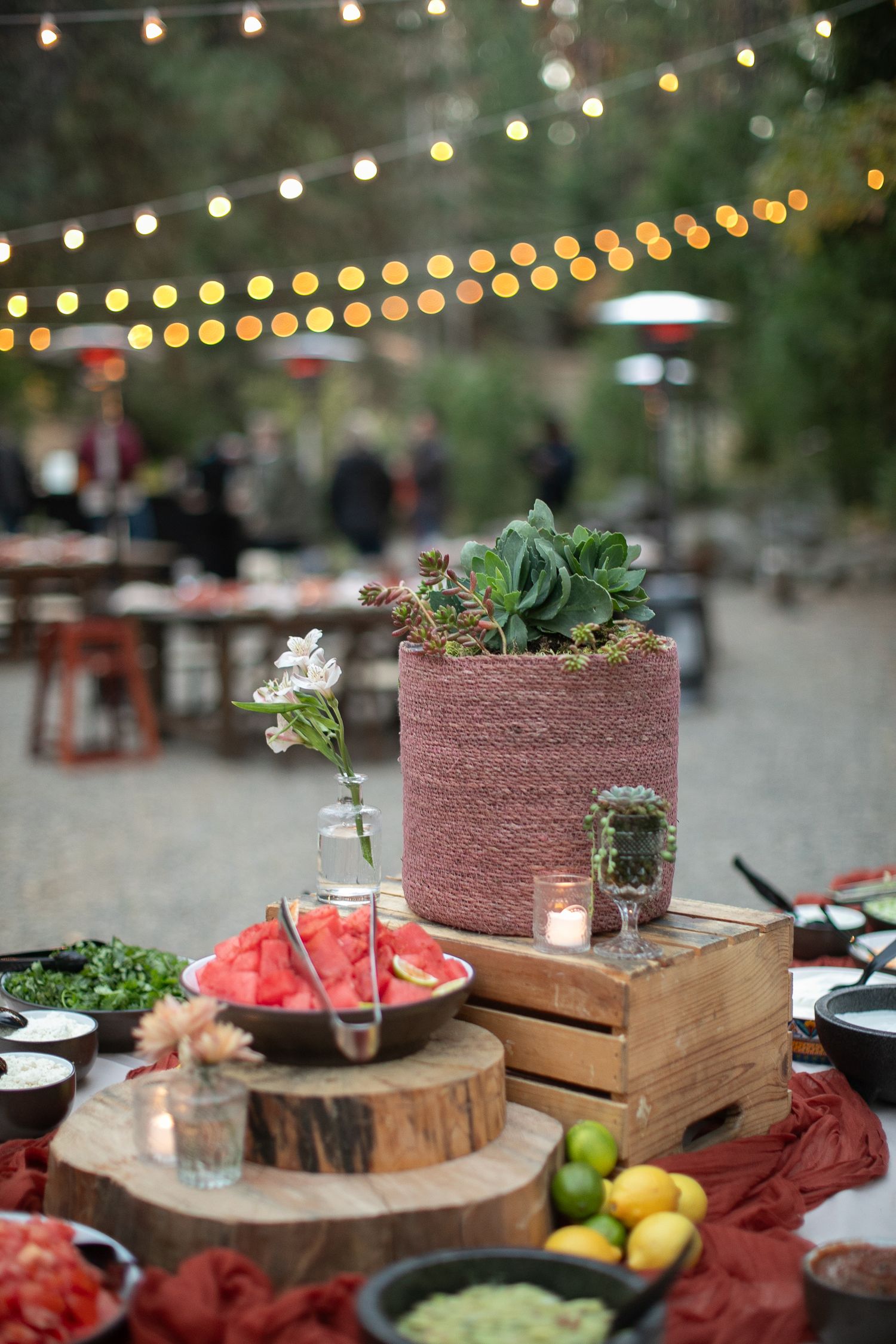 Outdoor party setup with string lights, wooden decor, and red table settings.