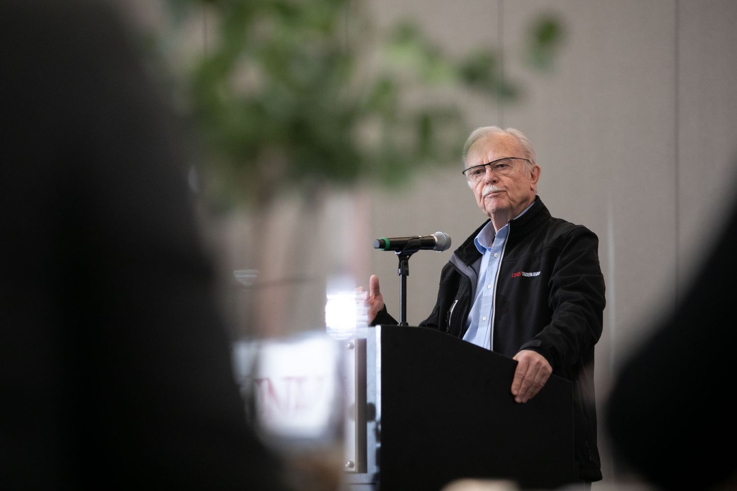A speaker addresses an audience from behind a podium at an indoor event.