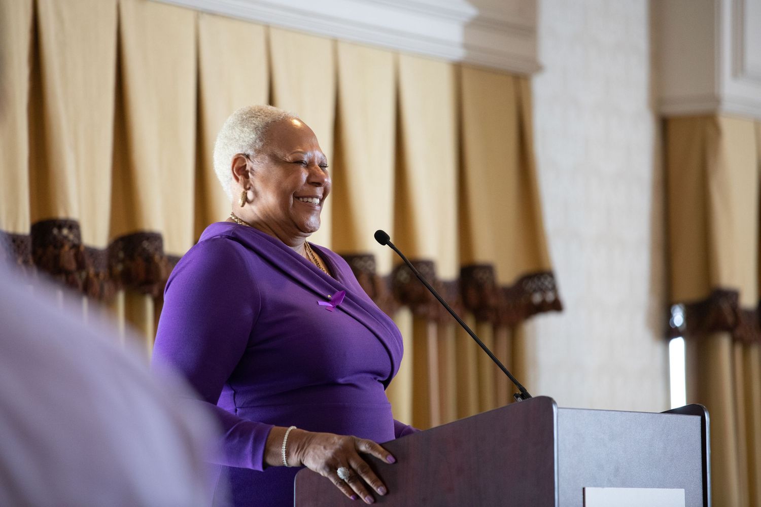 Speaker at podium wearing purple attire during formal presentation.