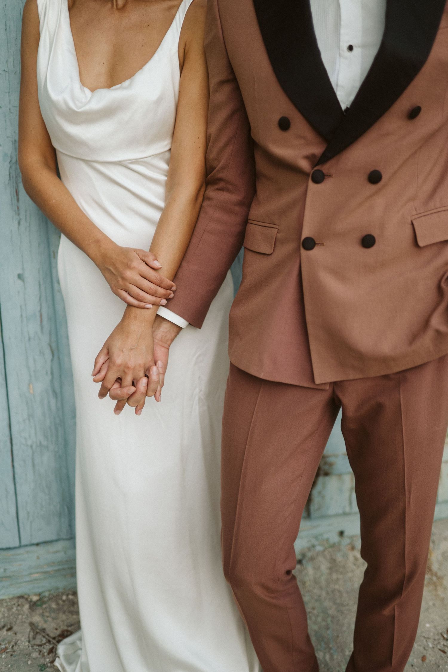 A couple holding hands wearing a white wedding dress and brown double-breasted tuxedo with black lapels.