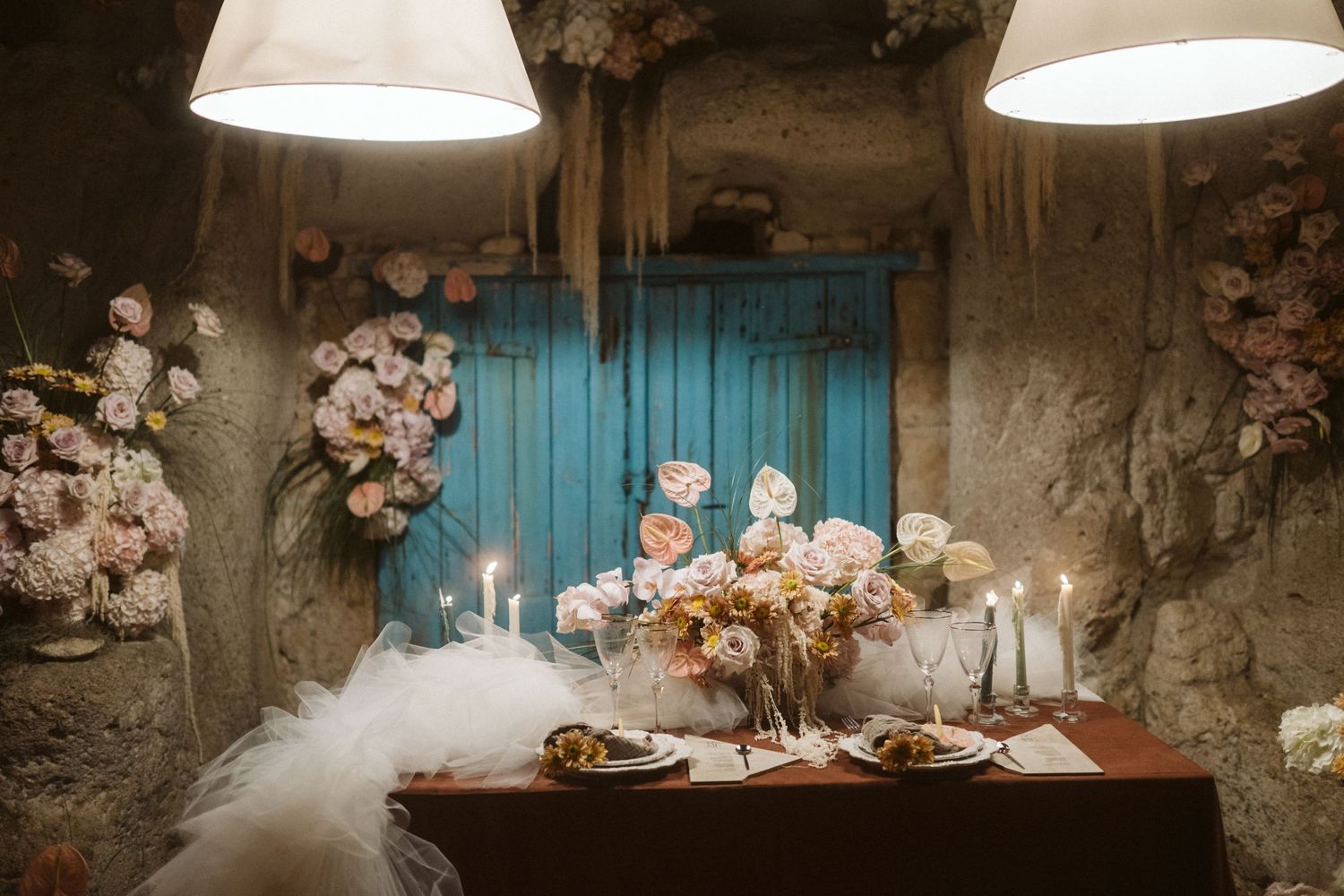 A romantic table setting with white flowers, candles and misty atmosphere against a rustic turquoise door backdrop.