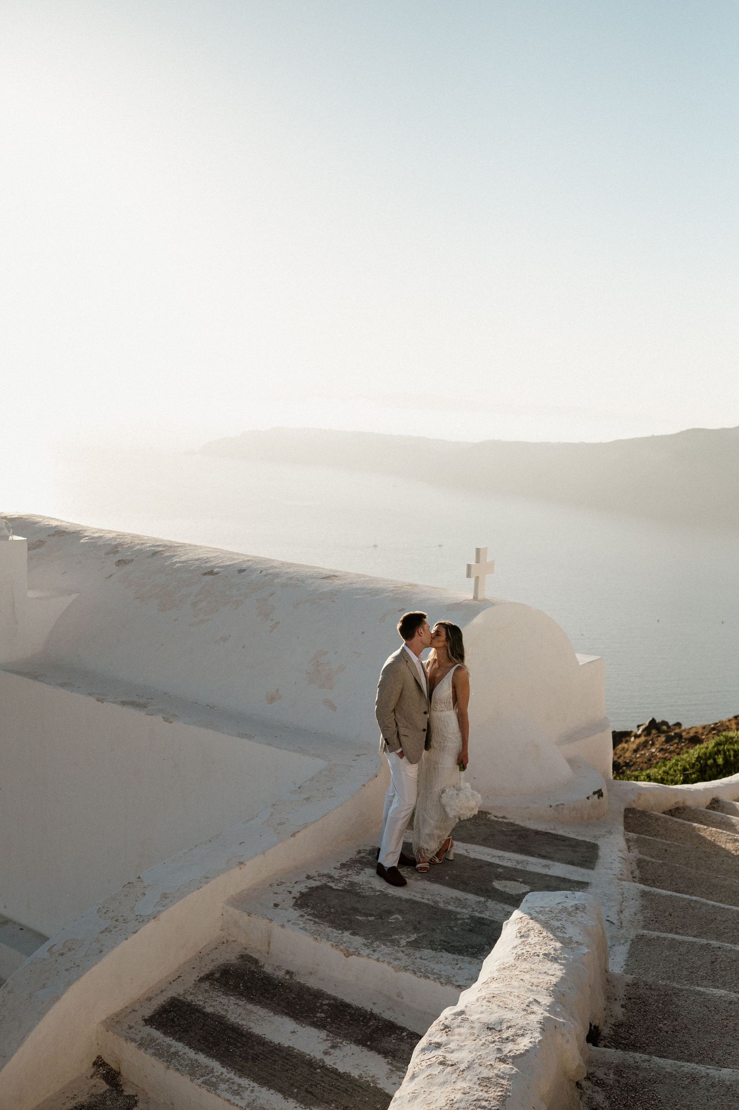 Romantic wedding scene on white steps overlooking Mediterranean sea.
