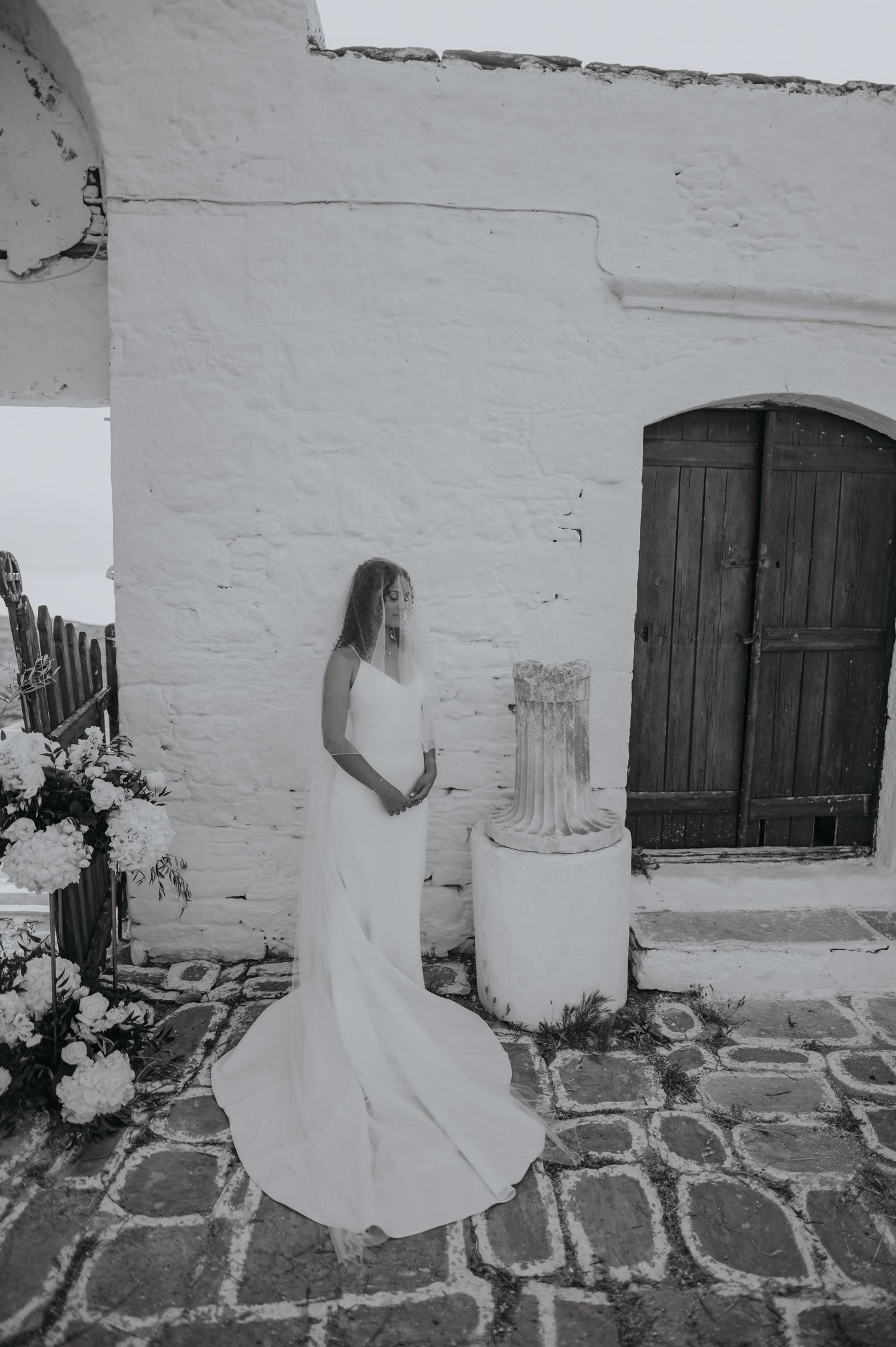 Black and white photo of a flowing white wedding dress against a Mediterranean style whitewashed wall and stone floor.