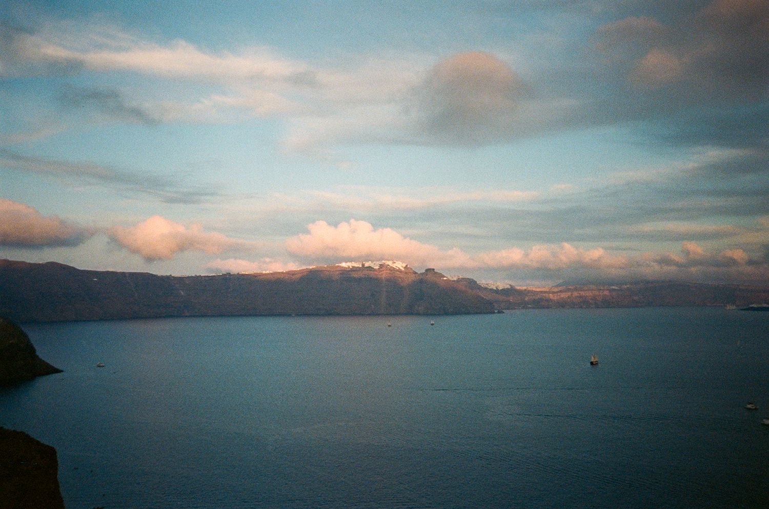 Scenic sunset view of a Mediterranean coastline with mountains and calm waters under pastel clouds.