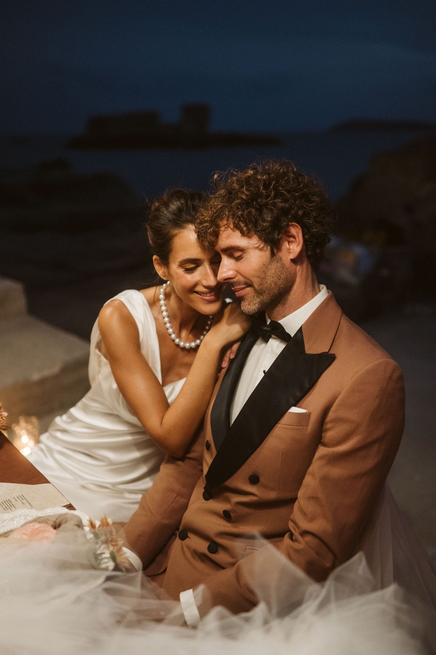 Romantic wedding couple shares an intimate moment at dusk in elegant evening attire.
