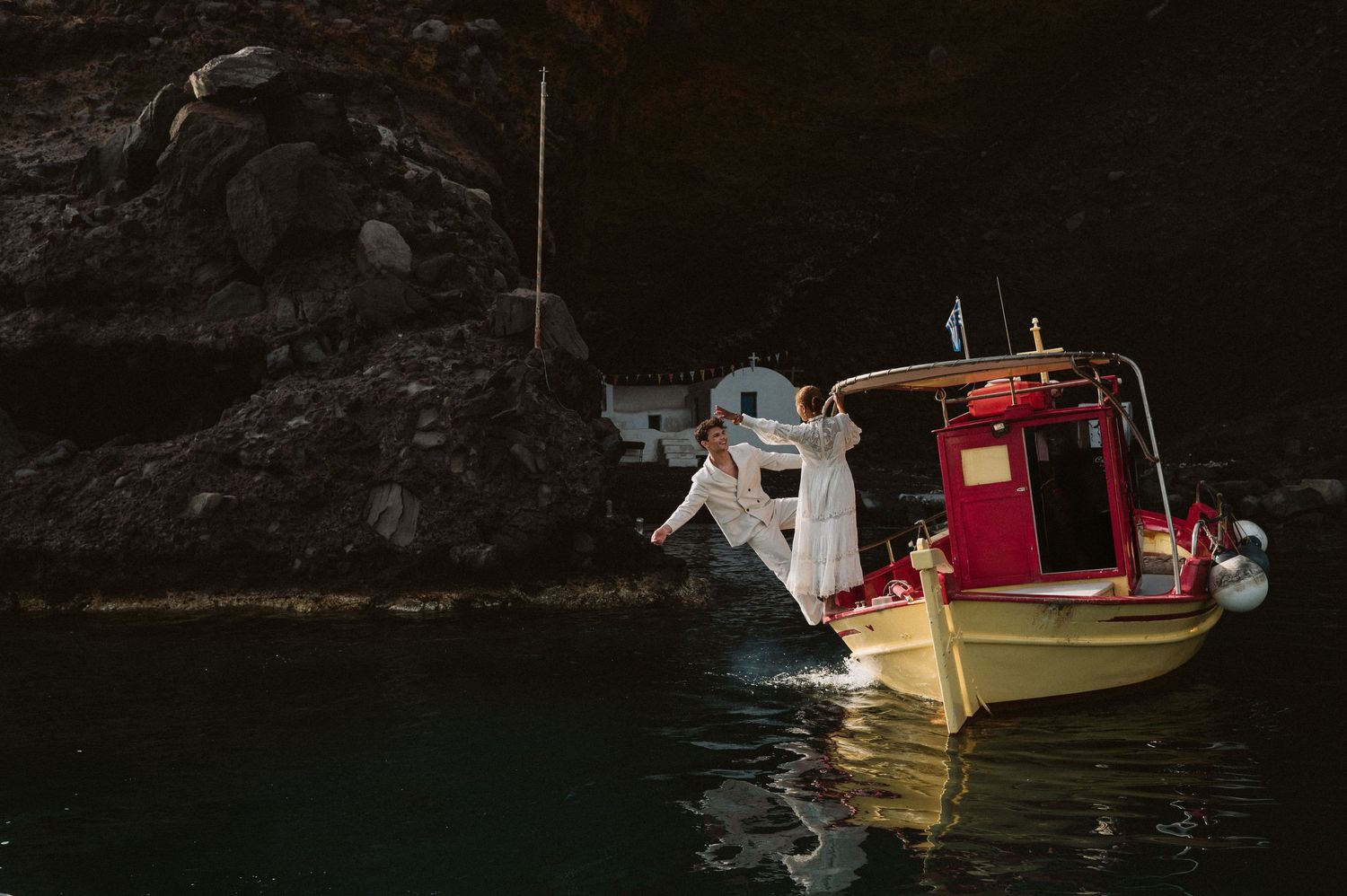 A yellow boat with red trim sits on dark waters against a rocky cliff backdrop.