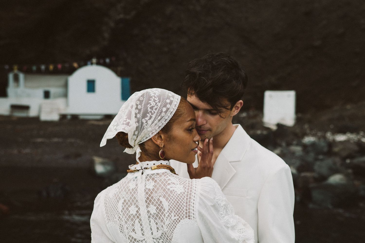 Traditional Mediterranean wedding scene with white lace details against village backdrop.
