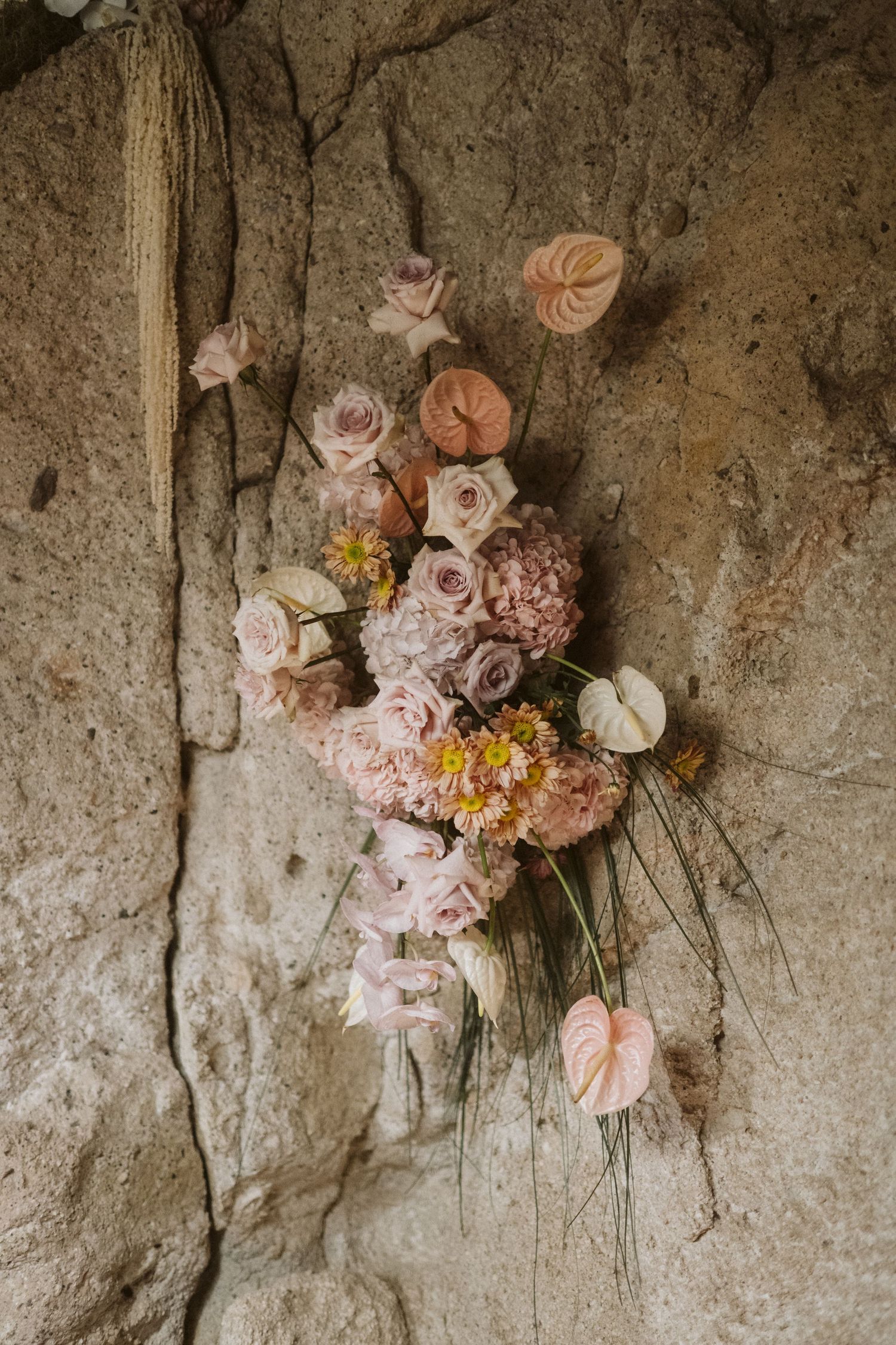 A romantic arrangement of pale pink roses and antique flowers laid against a textured stone wall background.