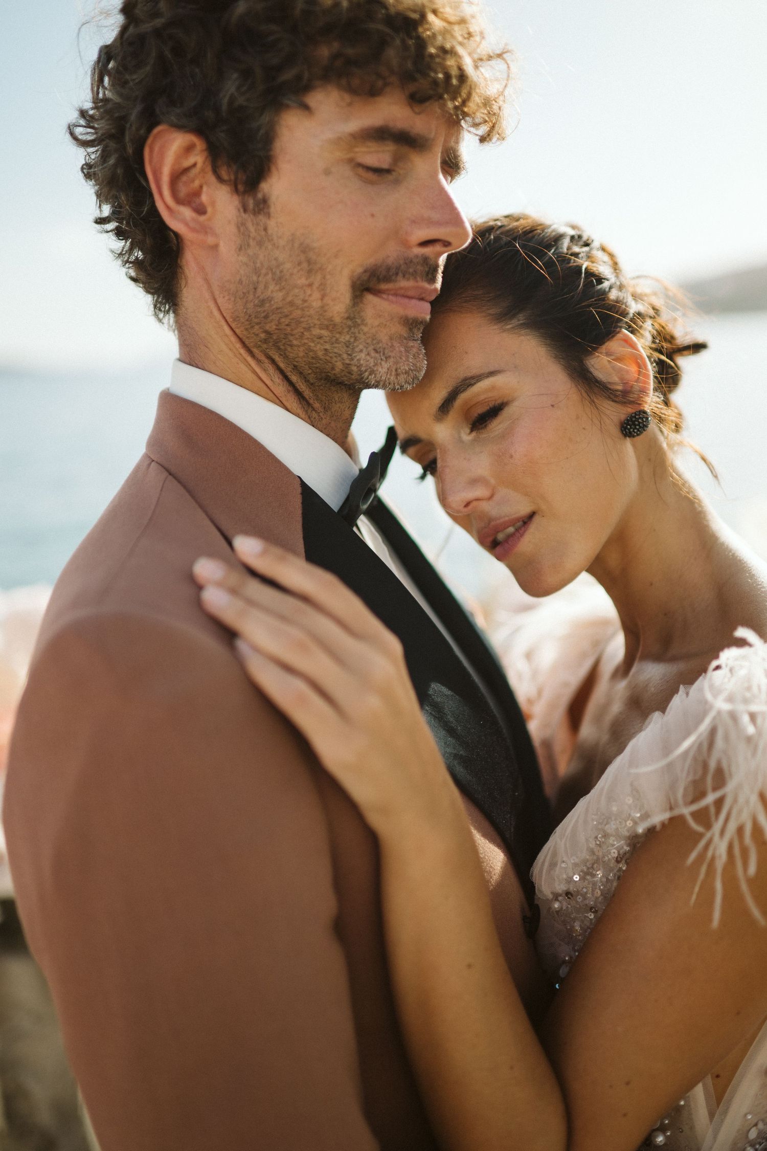 A bride and groom share an intimate moment in warm sunlight while embracing during their wedding photoshoot.