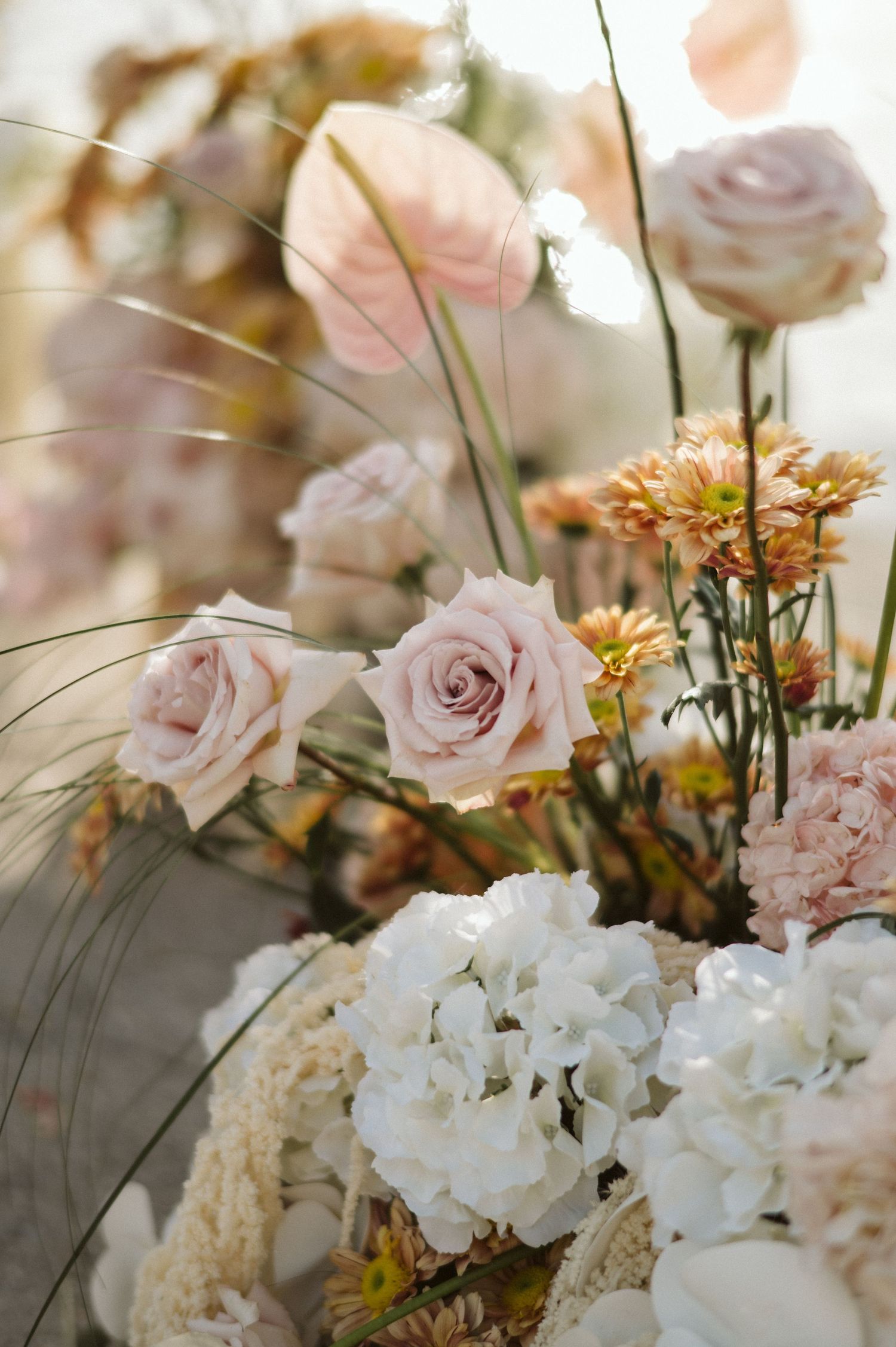 Soft pink roses and white hydrangeas arranged with delicate grasses and yellow flowers in a romantic floral display.