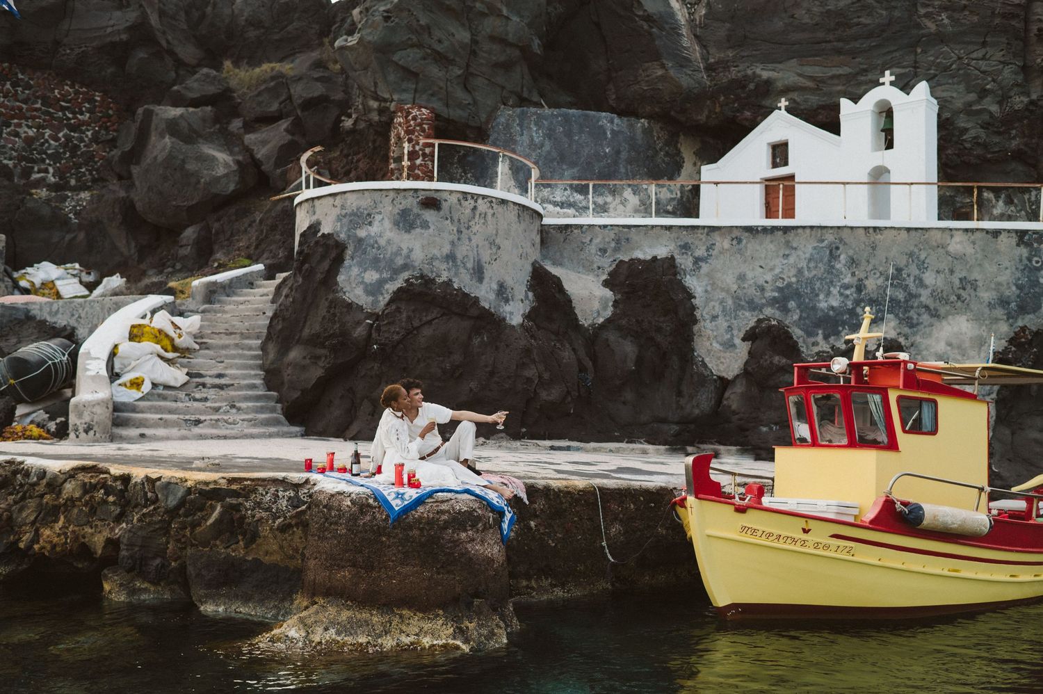 A yellow boat rests near white buildings and steps carved into dramatic coastal cliffs.