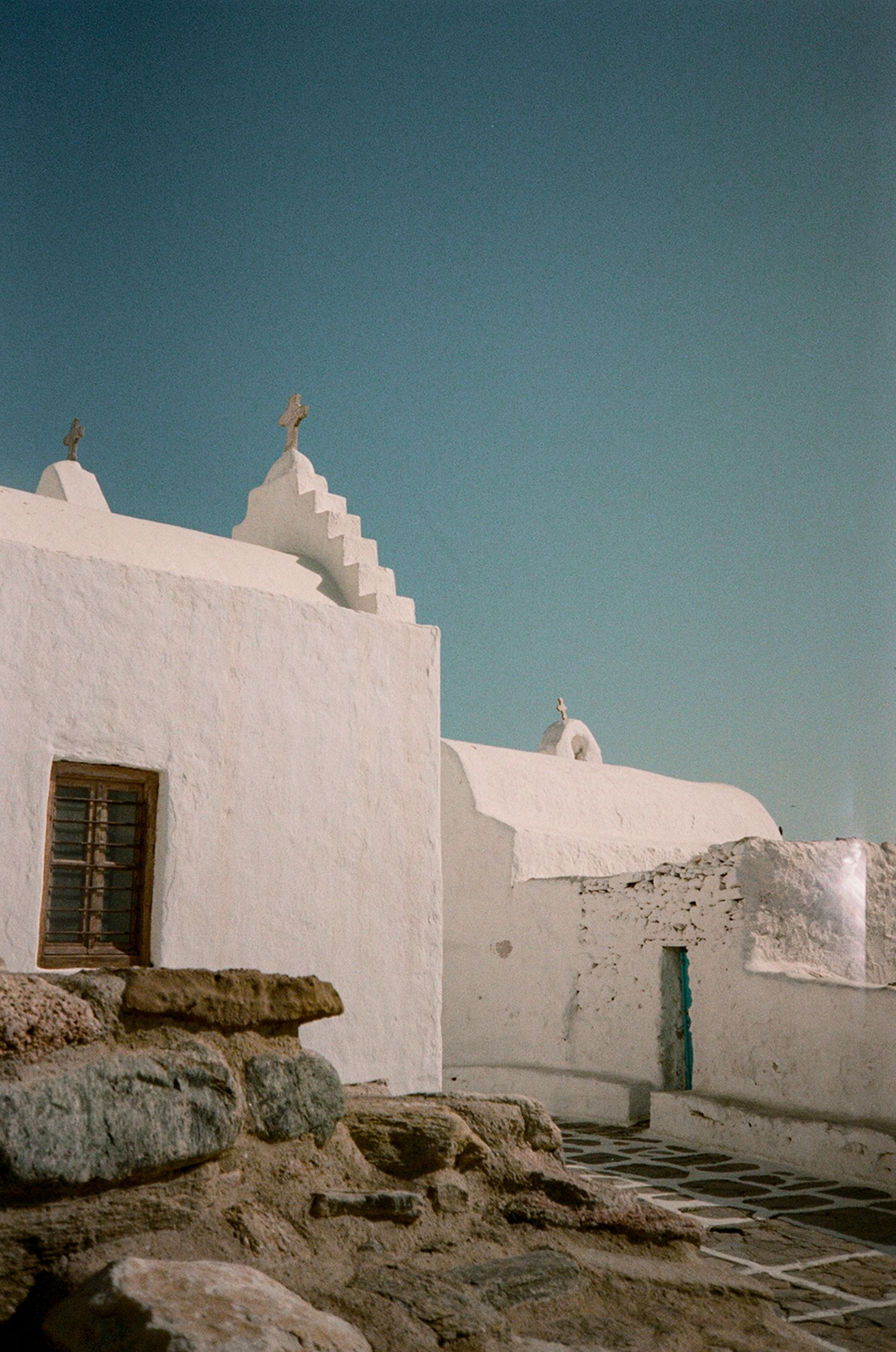 White adobe church buildings with stepped rooflines against a turquoise sky in a traditional Mediterranean style.