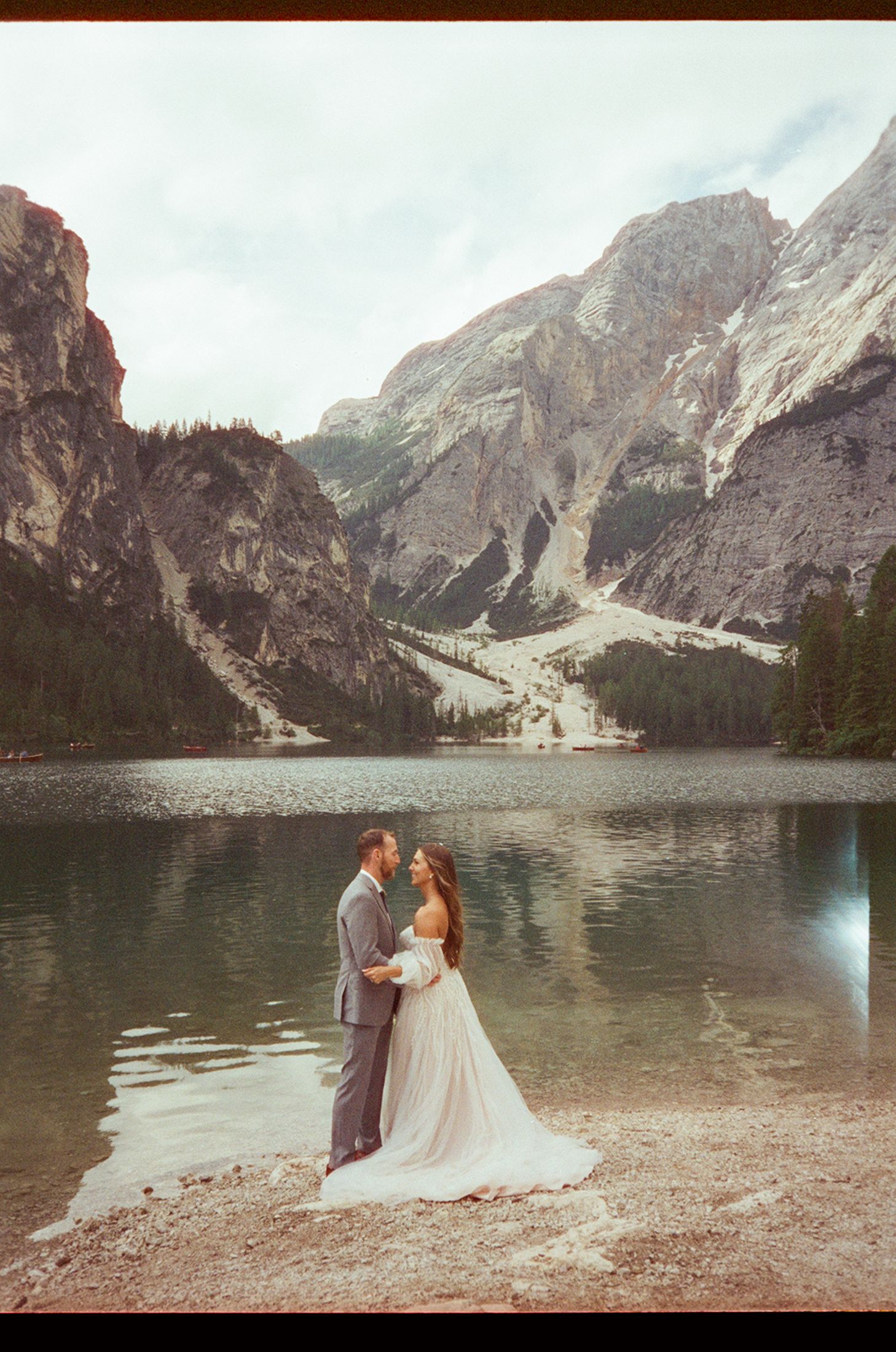 A romantic wedding photo sequence at a serene mountain lake surrounded by dramatic rocky cliffs and evergreen trees.