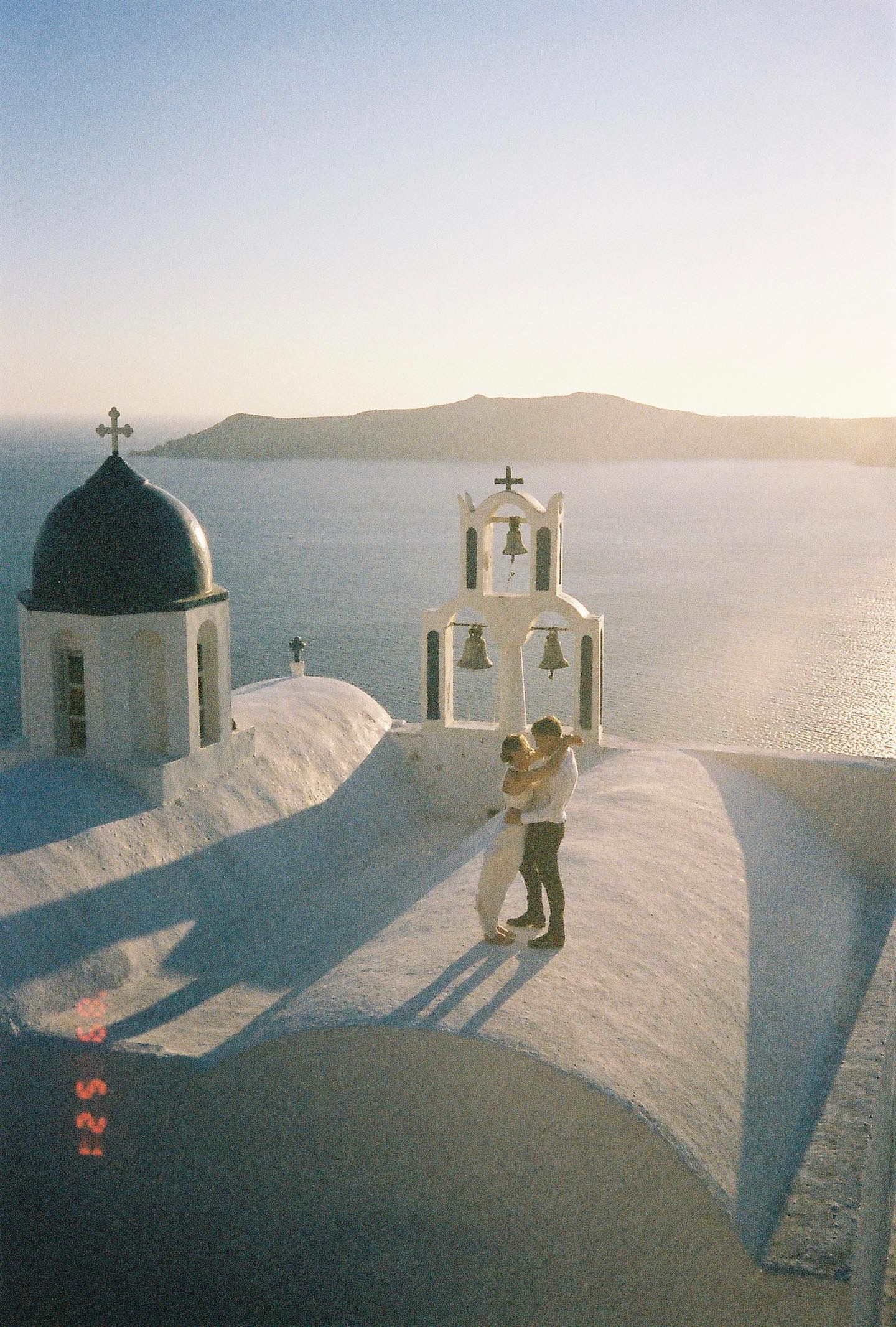 White domed churches with blue roofs perched on a cliff overlooking the Mediterranean Sea in Santorini at sunset.