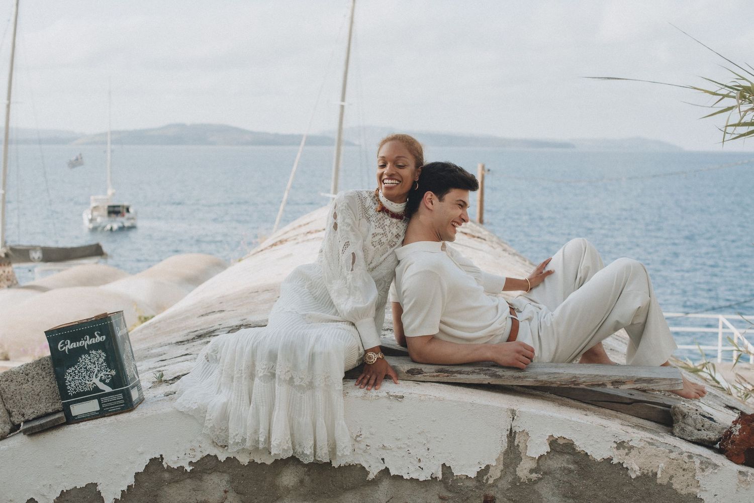 A couple lounges in white outfits on a seaside terrace with ocean views.
