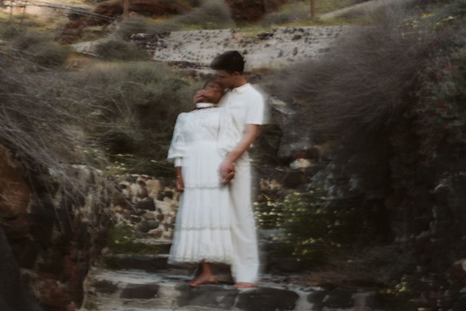 A couple embraces on stone steps in a dreamy, soft-focused outdoor setting.