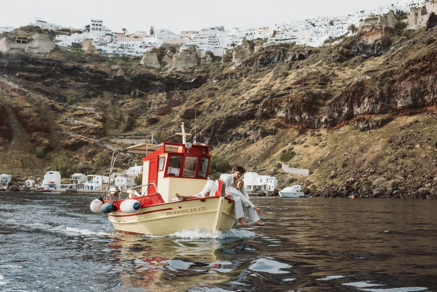 A small boat approaches whitewashed coastal buildings nestled into dramatic cliffs.