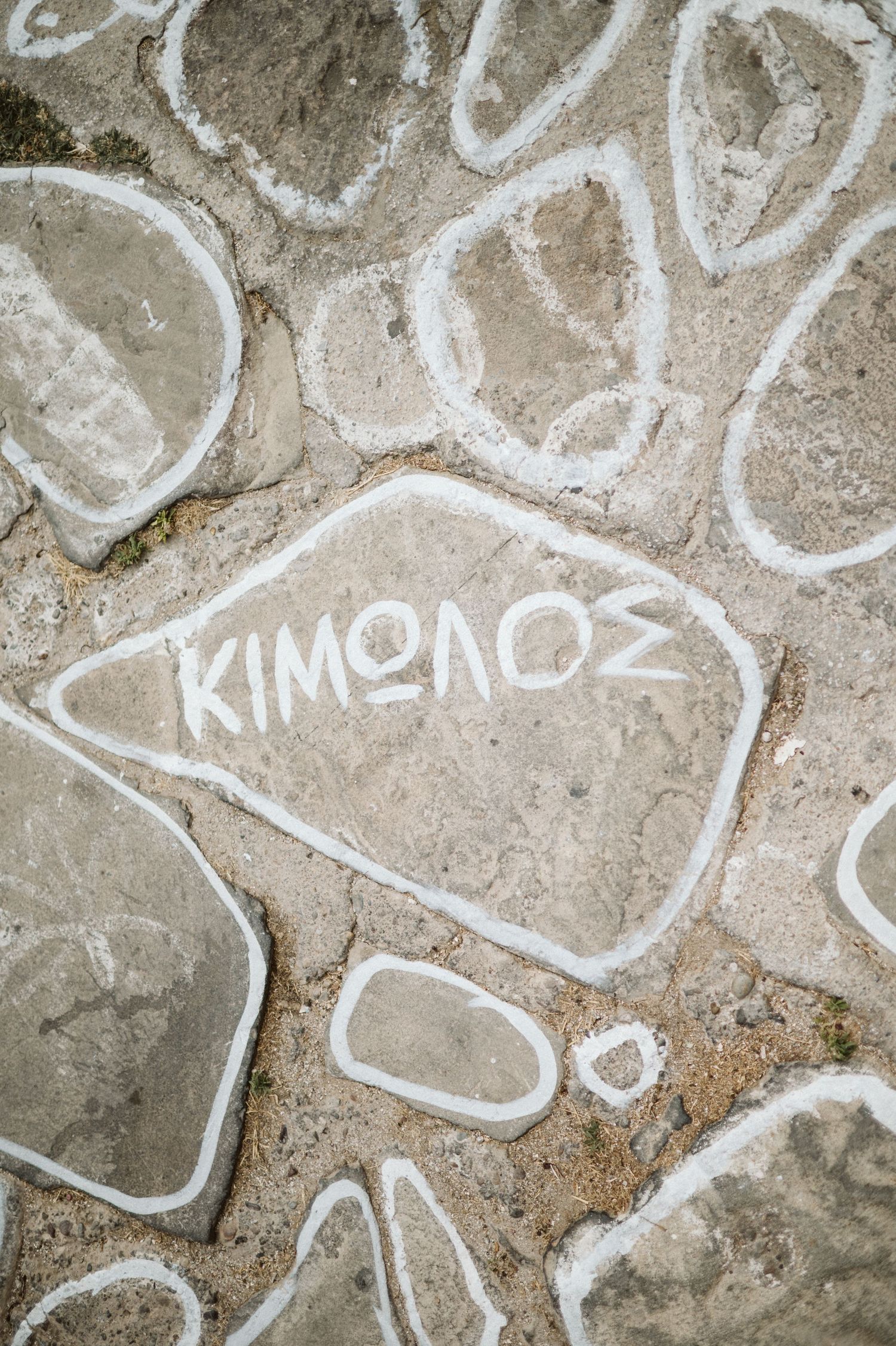 White chalk graffiti writing of 'KIMONOS' on gray concrete surface with abstract curved shapes drawn around it.