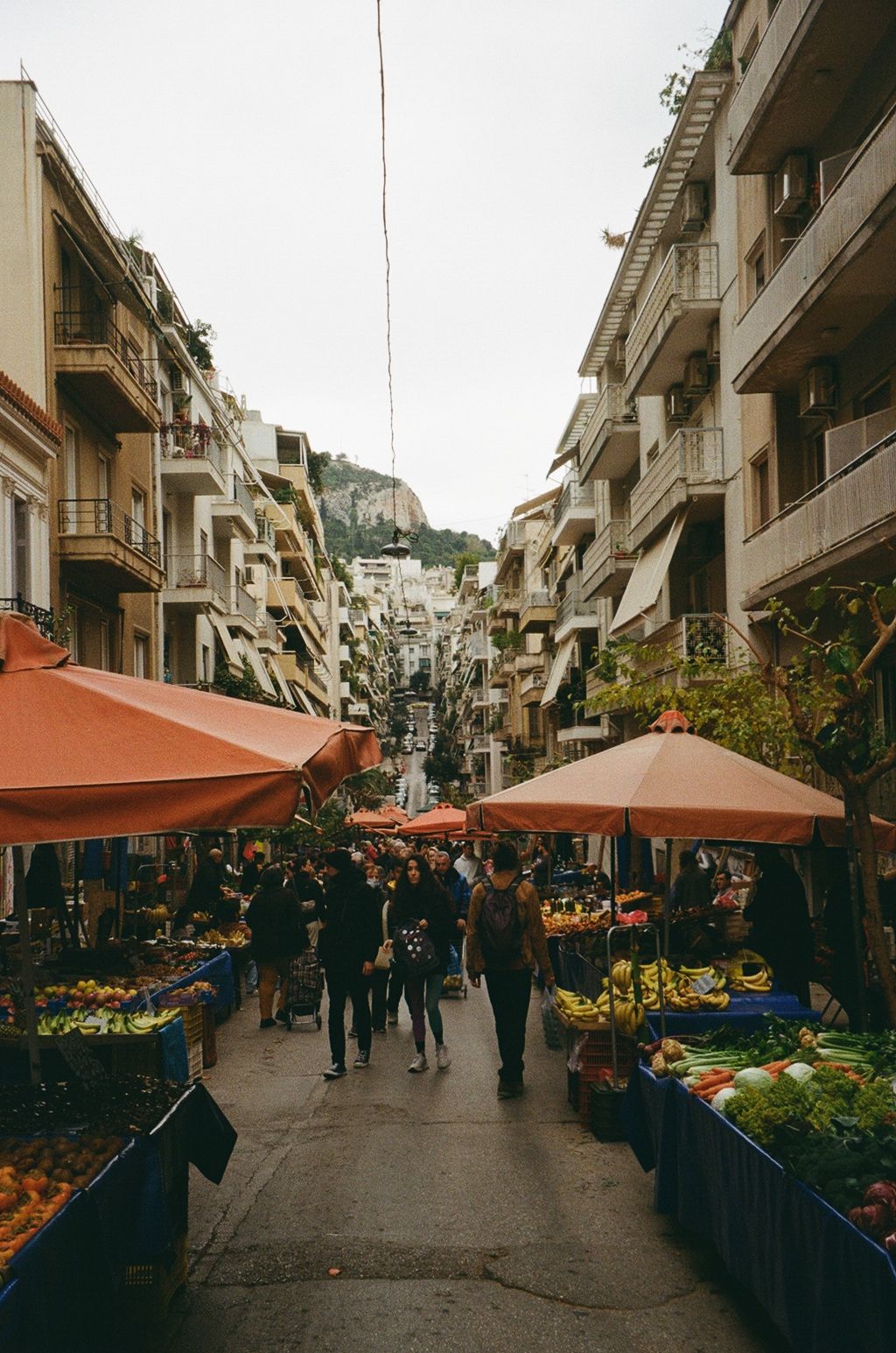 Outdoor street market in Mediterranean town with flower stalls and vendor booths under orange awnings.