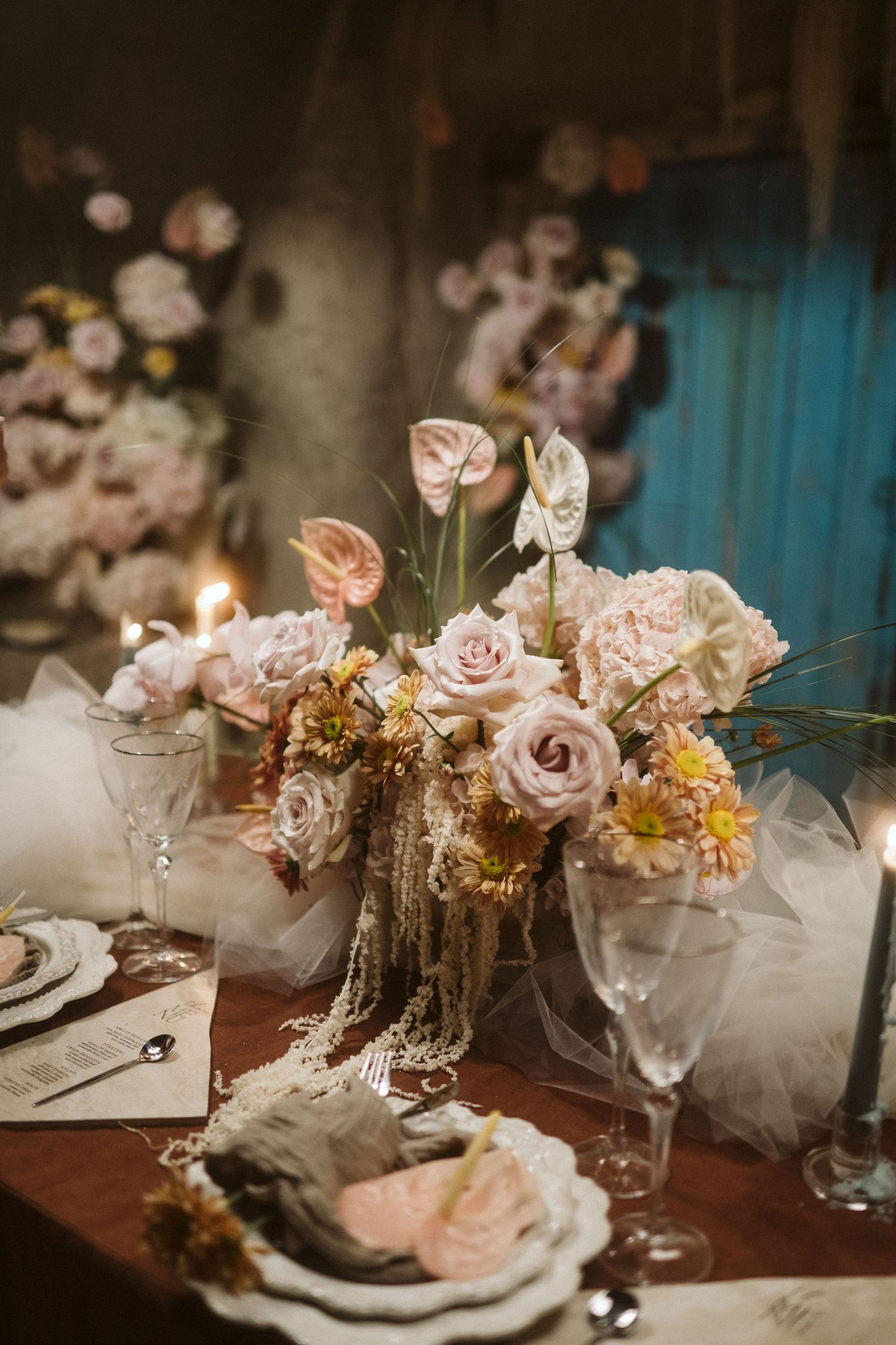 Elegant wedding table centerpiece with blush roses and crystal glassware in moody vintage lighting.