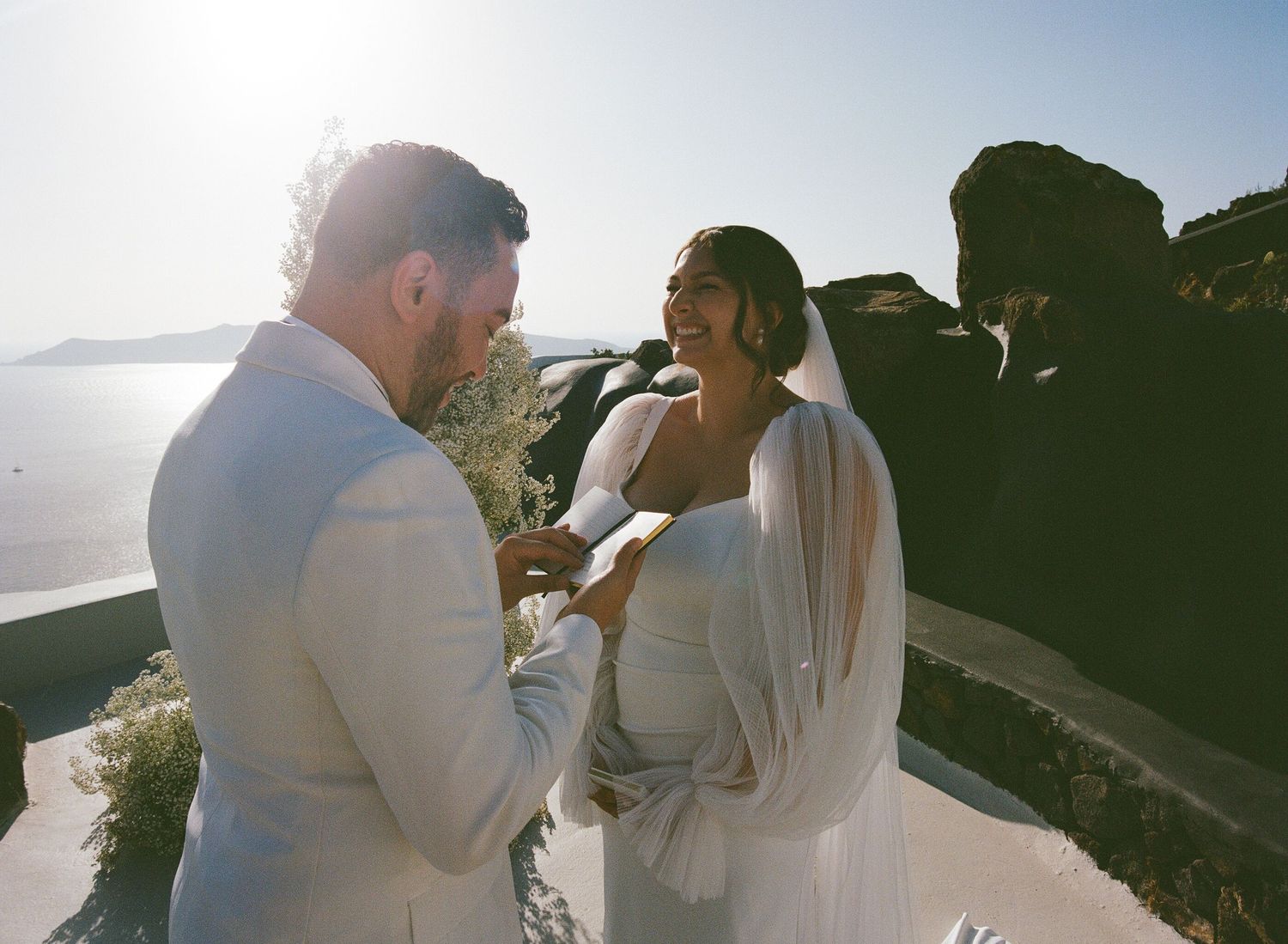 A couple in white wedding attire shares romantic moments at sunset on a mountain overlook.