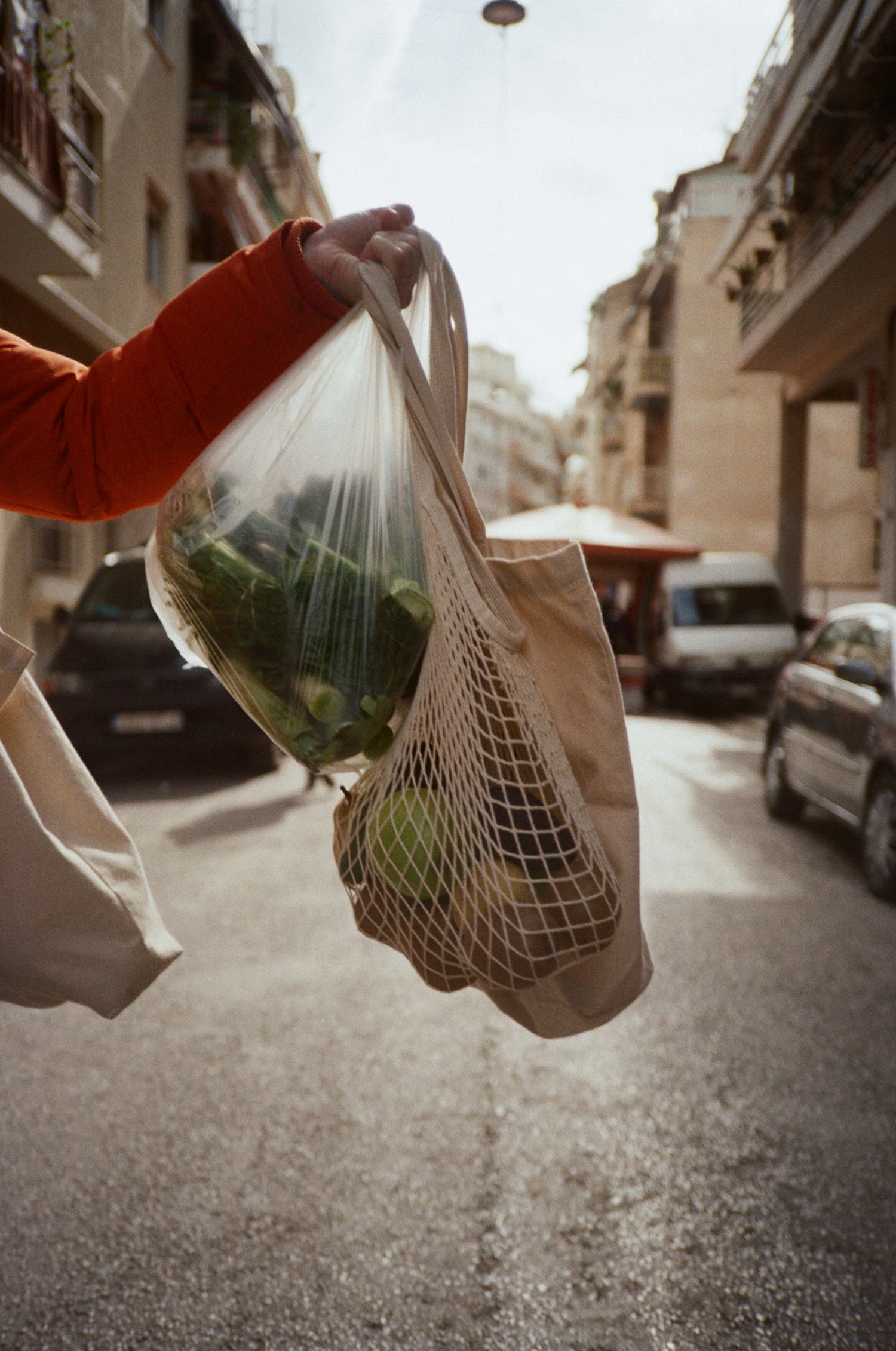 A sequence of mesh grocery bags swinging in motion against an urban street backdrop with parked cars and buildings.