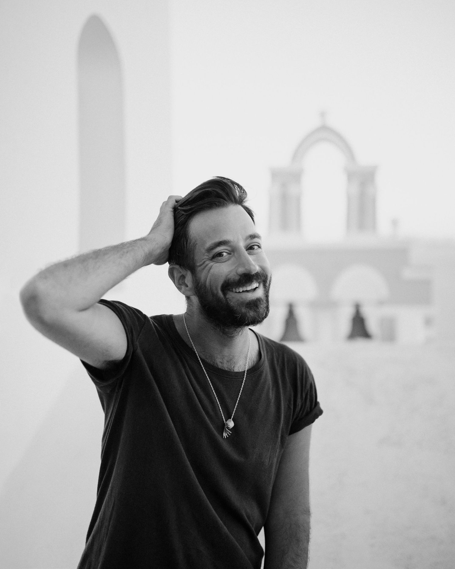 Black and white portrait of me in a t-shirt smiling against a white Mediterranean architectural background.
