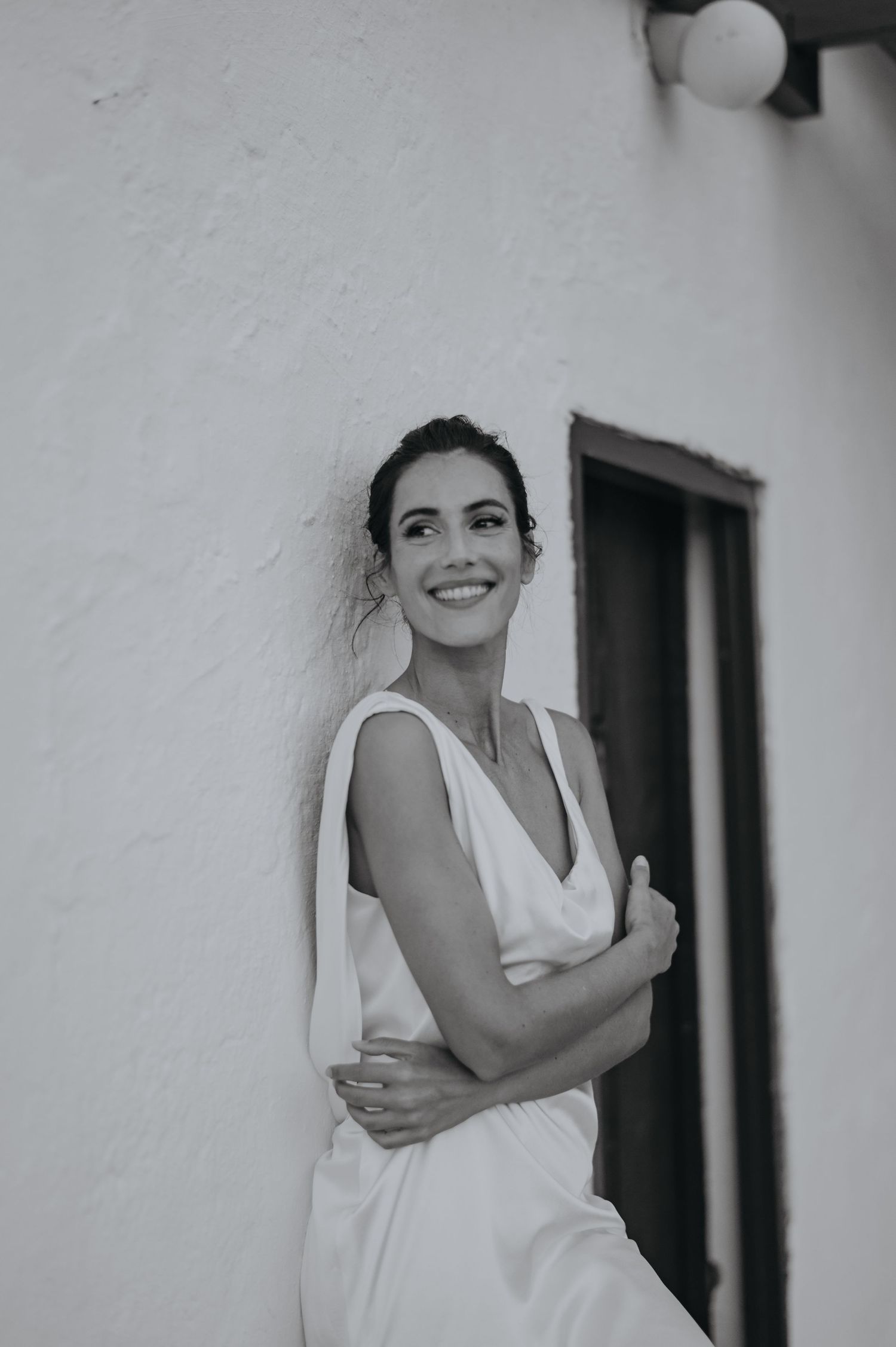 Black and white portrait of someone in a white dress smiling against a light-colored wall.