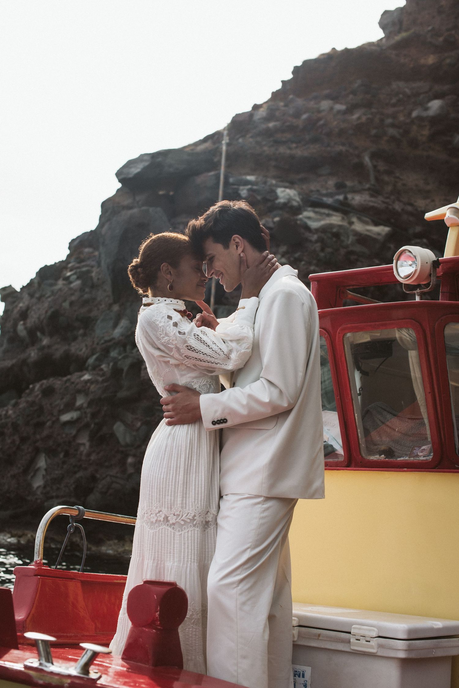 Romantic embrace on a red and yellow boat against dramatic coastal cliffs.