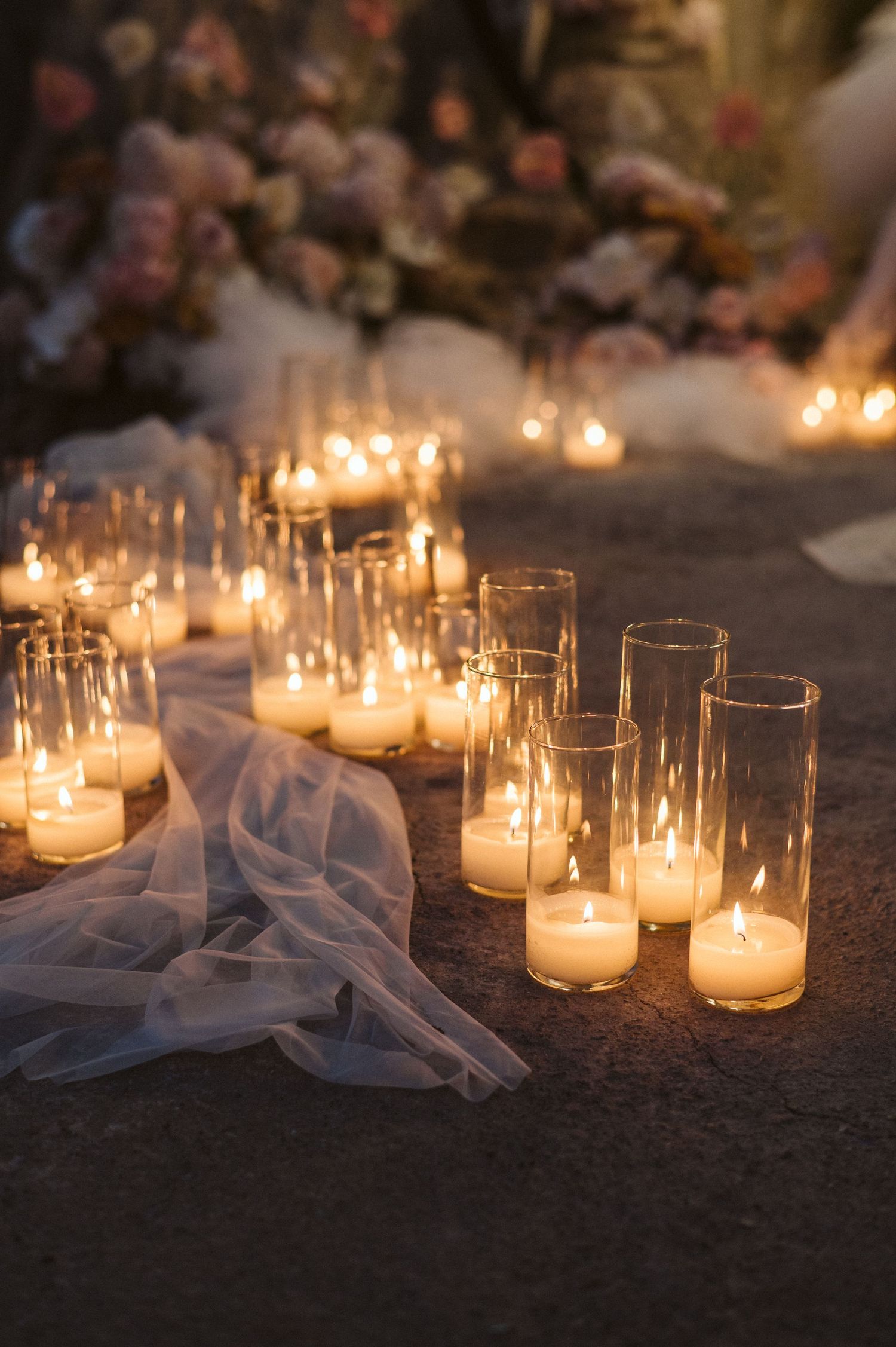 Glowing candles in glass votives line up along delicate white tulle fabric creating a romantic ambiance.