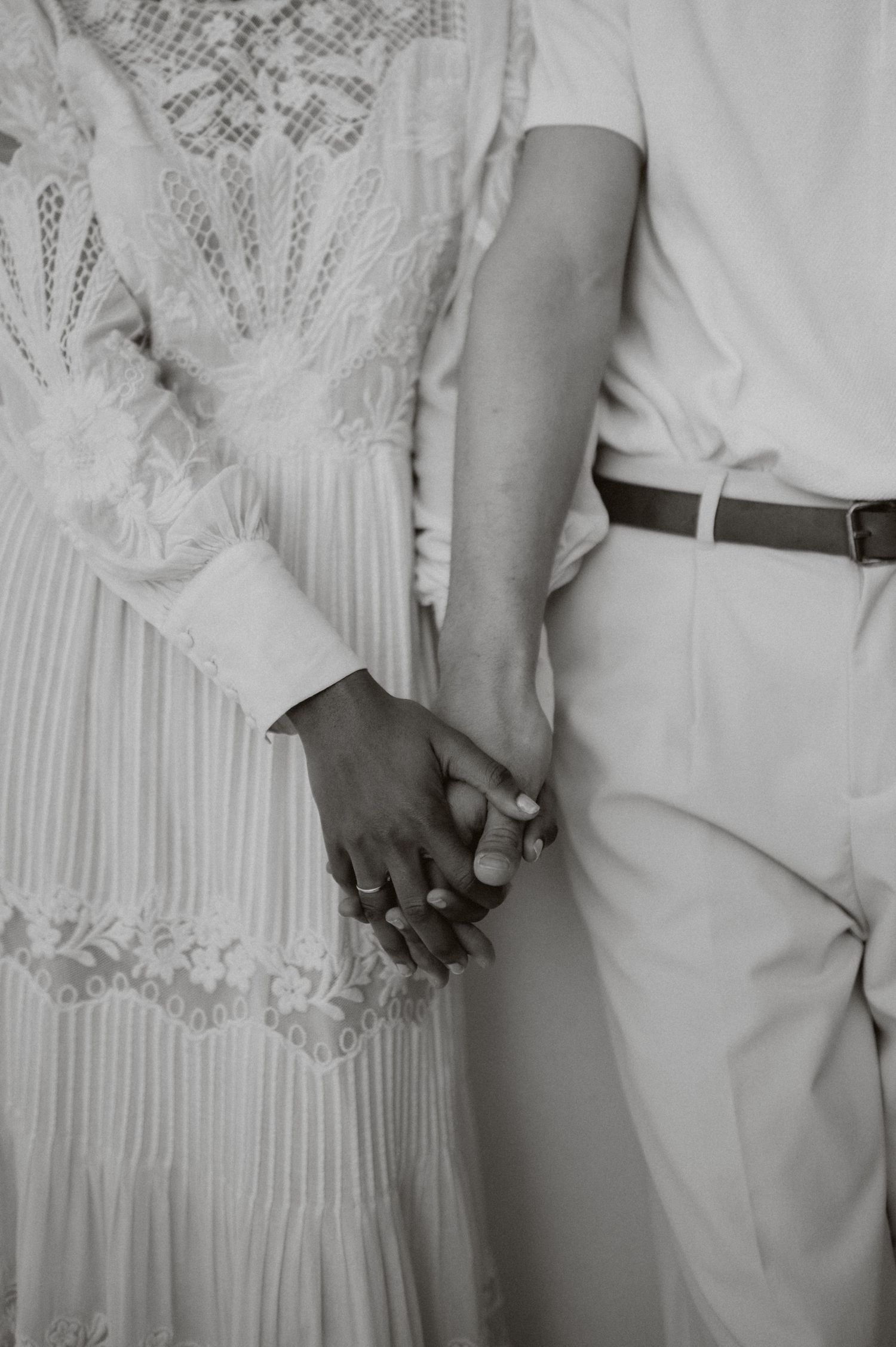 Close-up of hands clasped together showing white lace dress and light-colored suit details.
