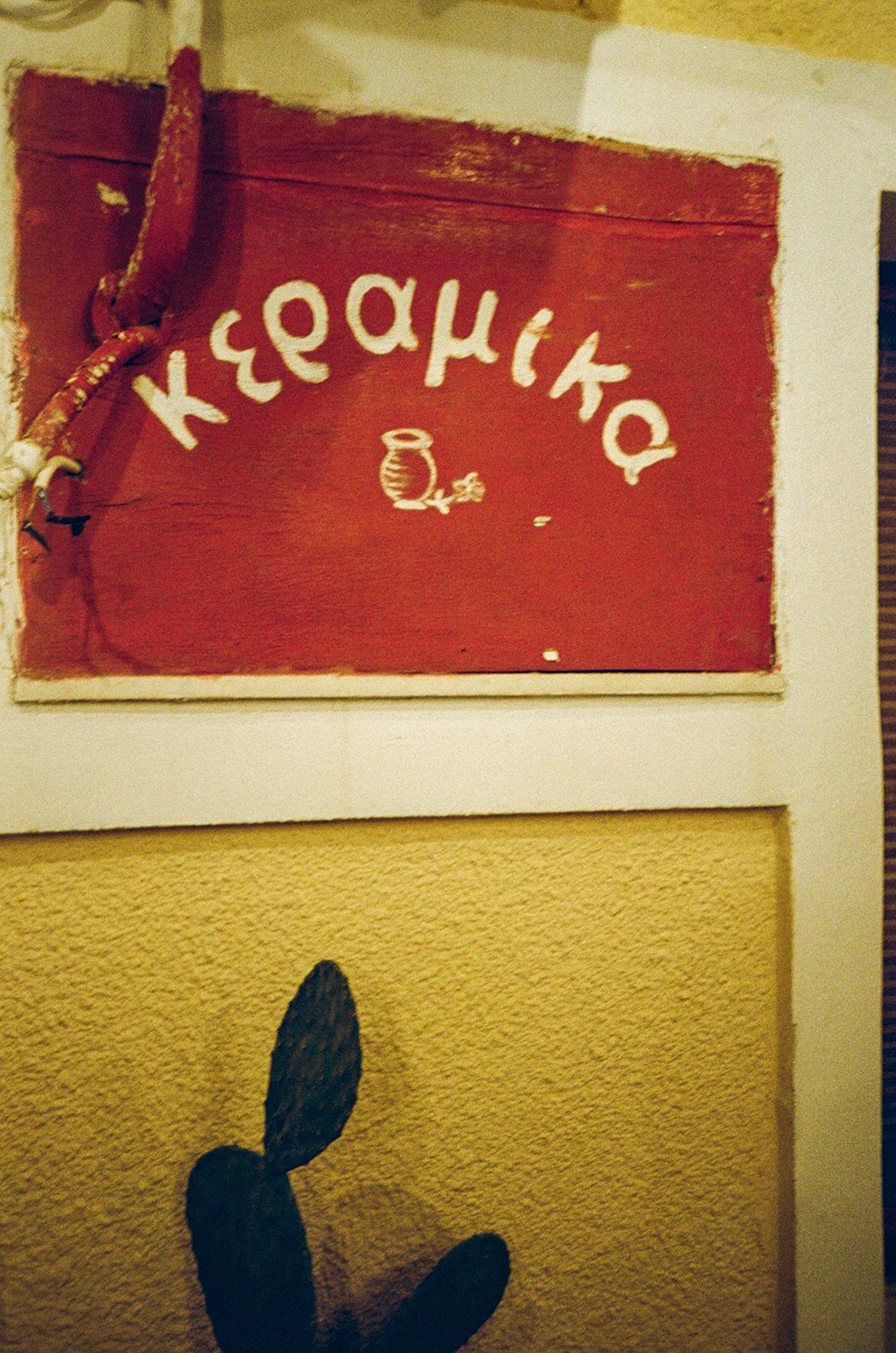 Red banners with Greek text hang on a yellow wall in what appears to be a cultural or community space.