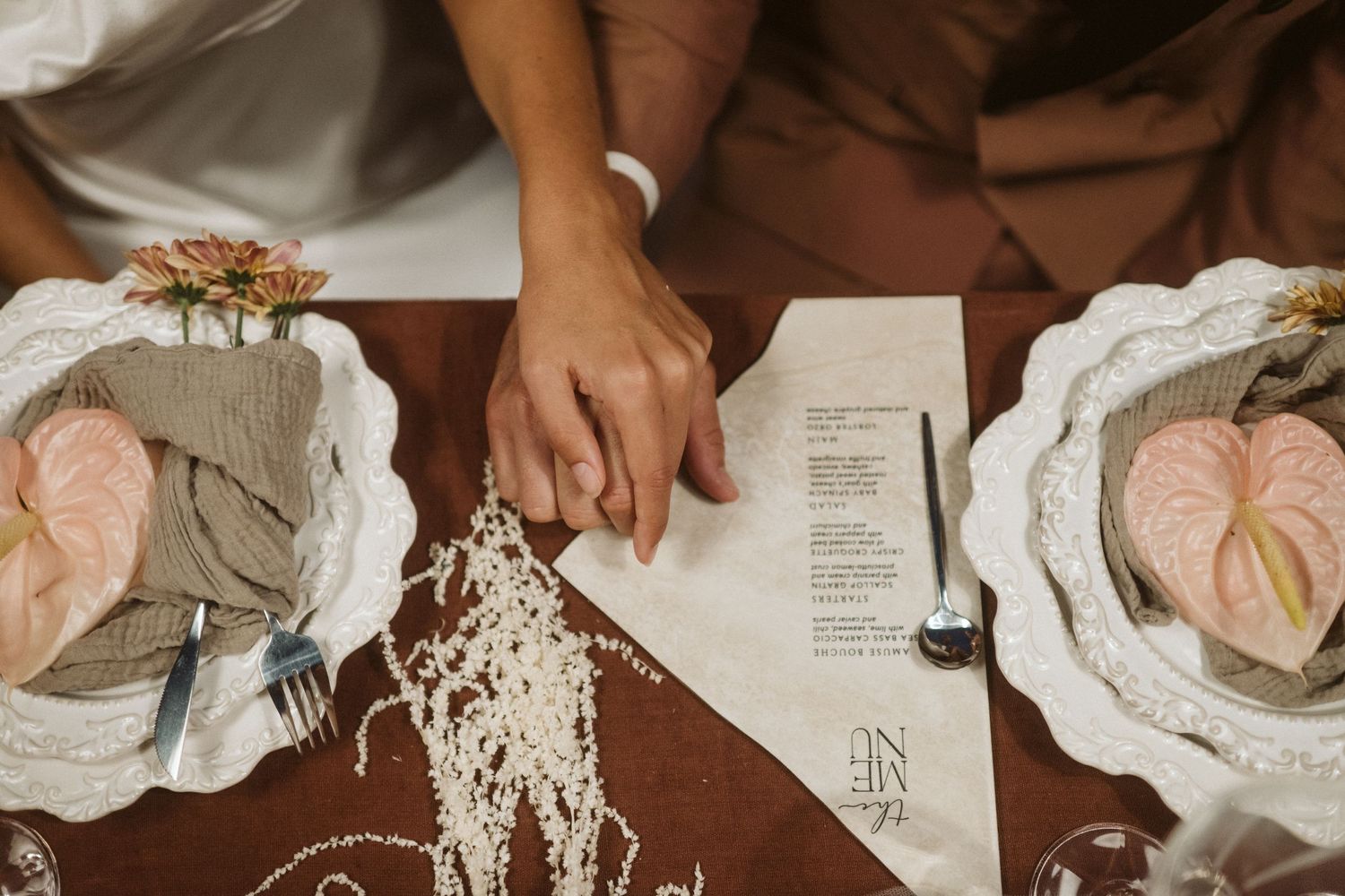 Overhead view of place settings with pink flowers and paper documents on a dark wooden table.