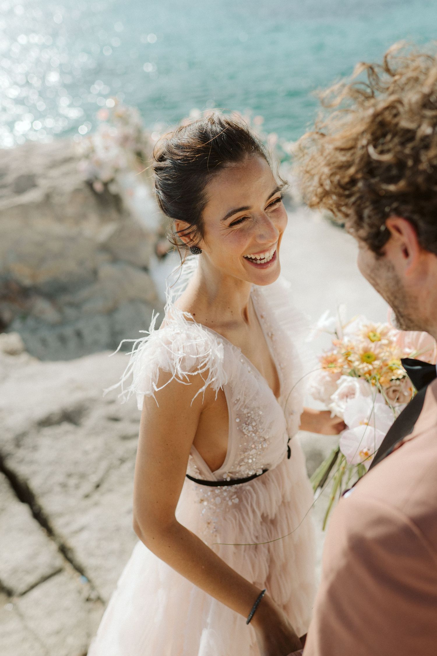 A romantic wedding moment captured seaside with soft sunlight and turquoise waters in the background.