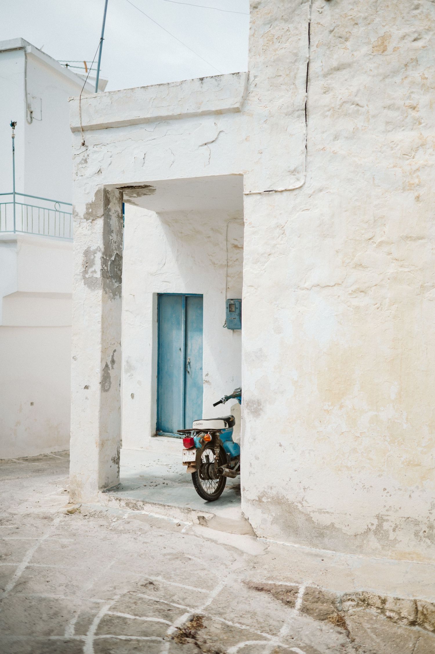 A vintage motorcycle parked in a whitewashed Mediterranean alleyway with a turquoise blue door.