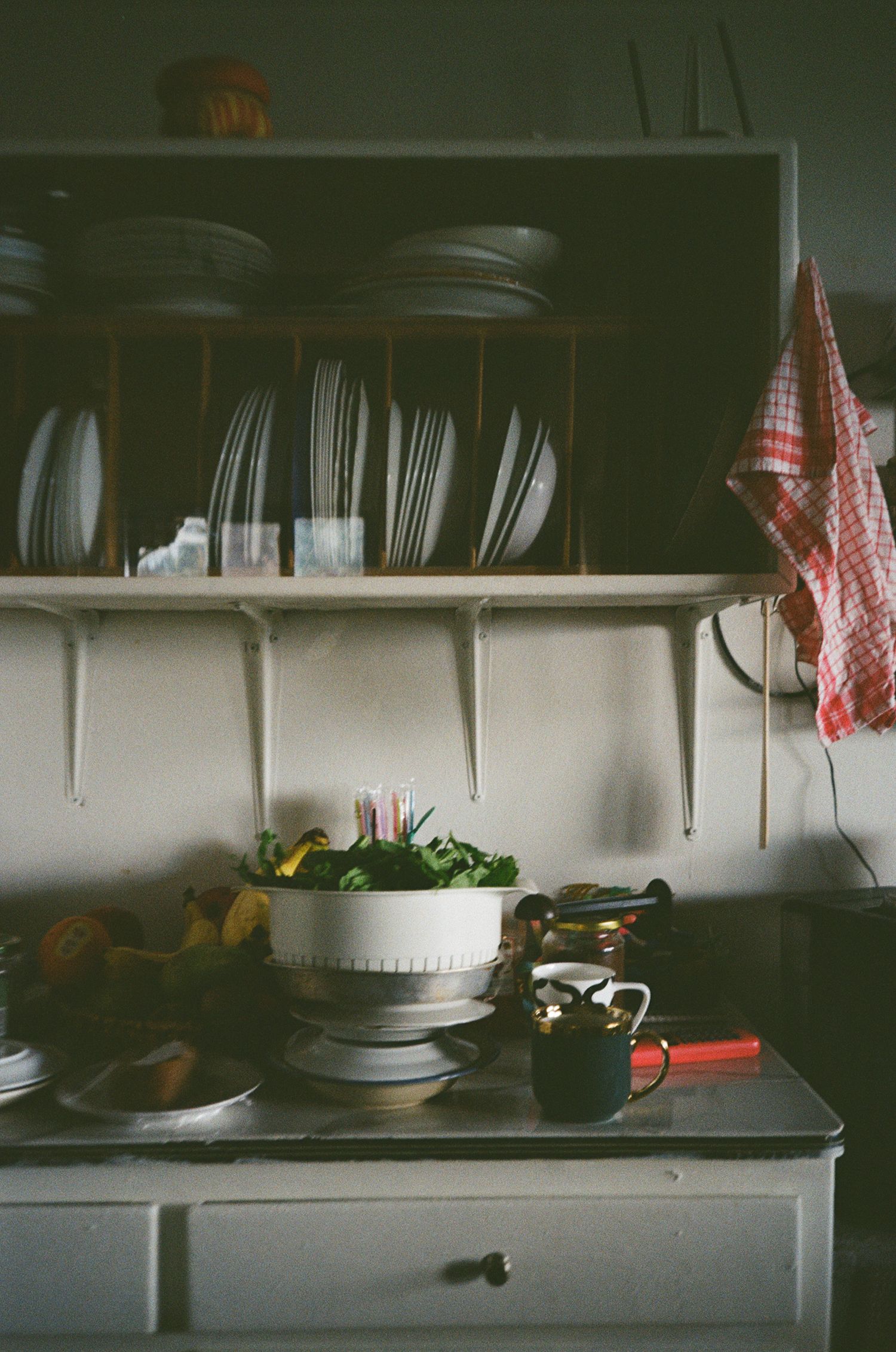 A dark moody kitchen counter scene with dishes and plates arranged against white cabinets in vintage style lighting.
