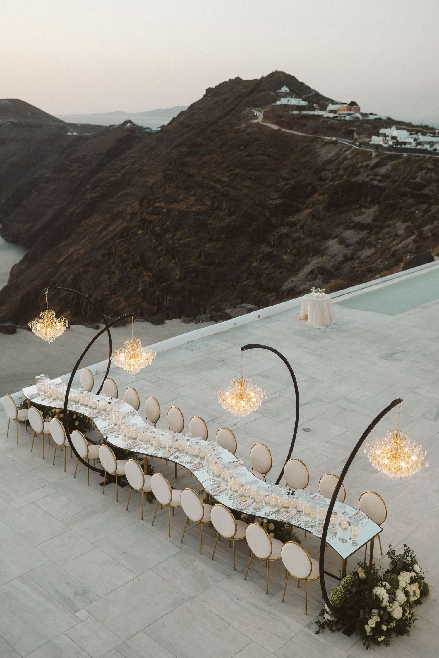Elegant outdoor wedding reception table setup overlooking dramatic coastal cliffs at sunset.