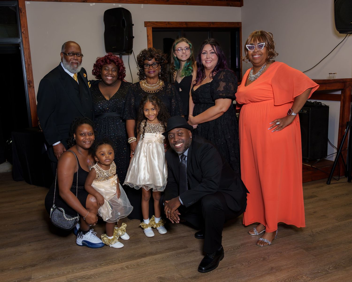 Large family group posing together at a formal indoor celebration event with speakers in background.