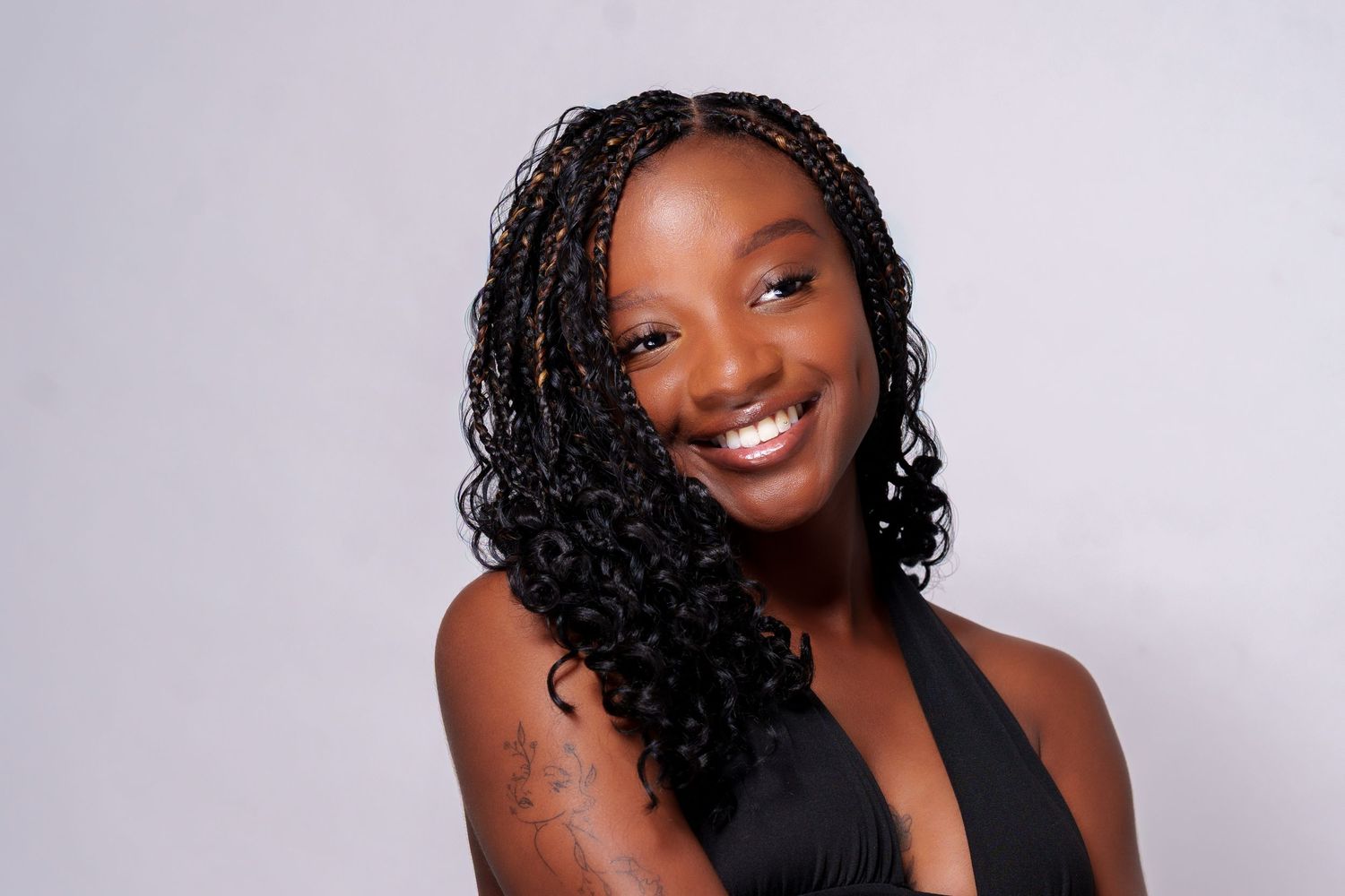 Smiling young woman with braided hairstyle wearing a black top poses against a gray background.