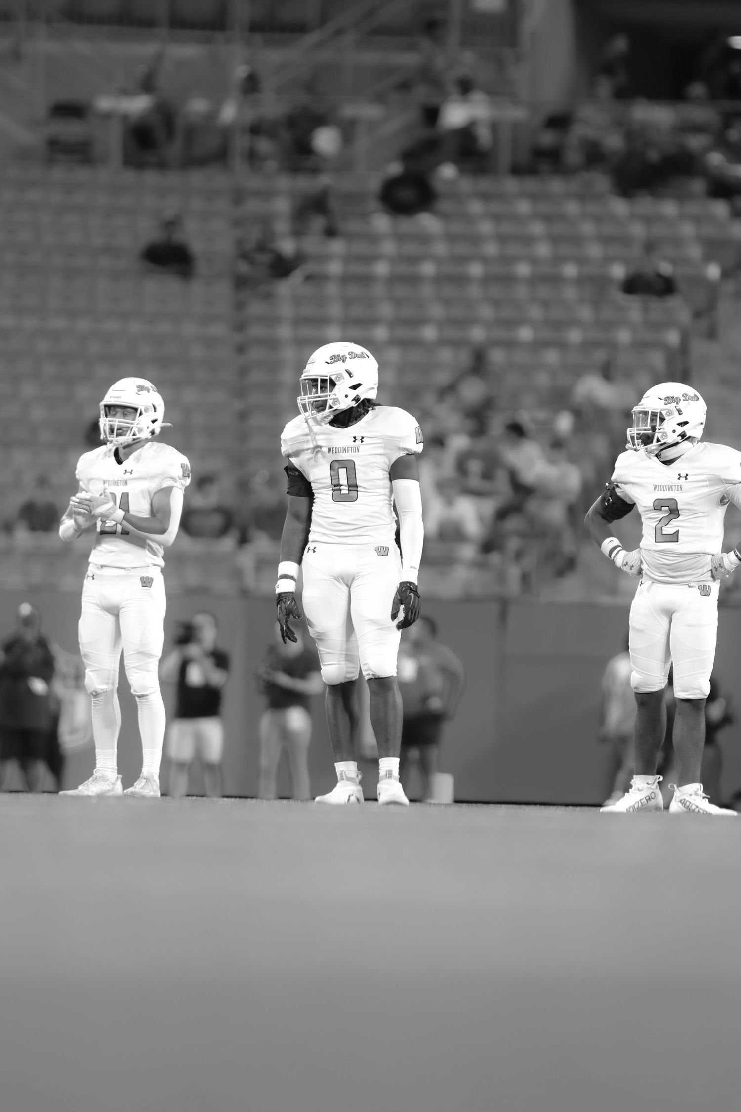 Black and white photo of three college football players in white uniforms standing on field during game.