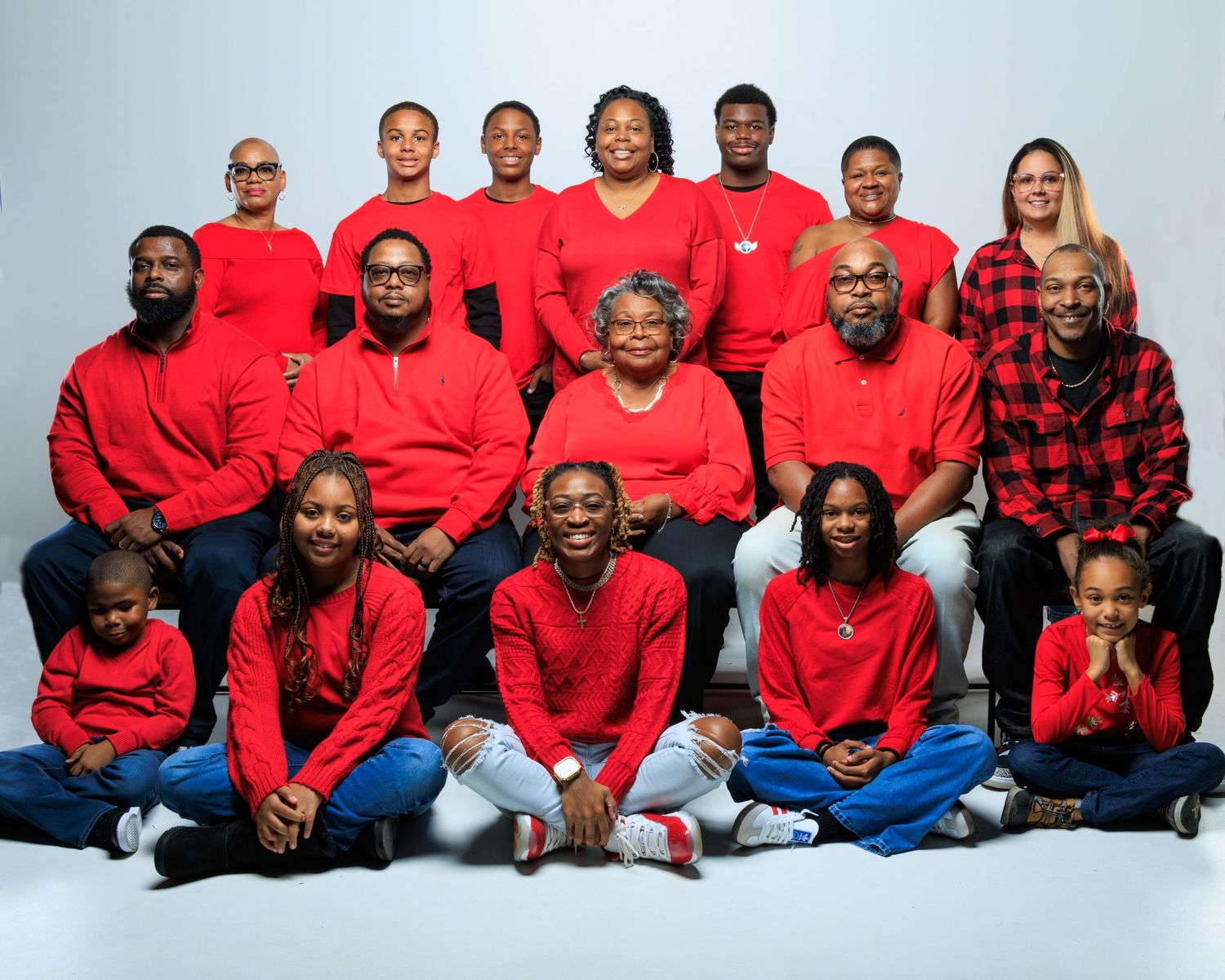 Large family group portrait in matching red outfits posing together on white background.