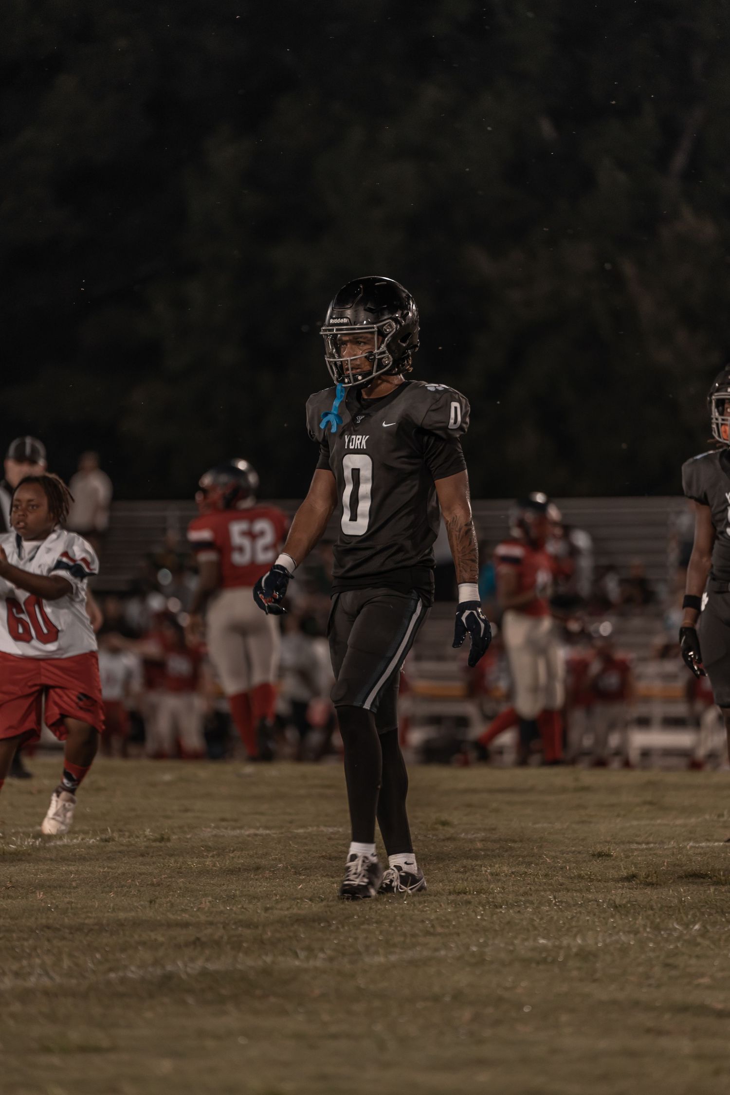 Football player wearing number 0 in black uniform walks on field during a night game.