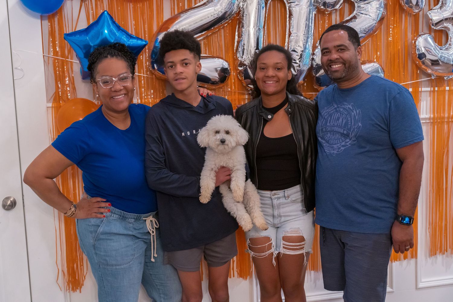 Family of four posing with a white poodle in front of 2023 balloon decorations at a party.
