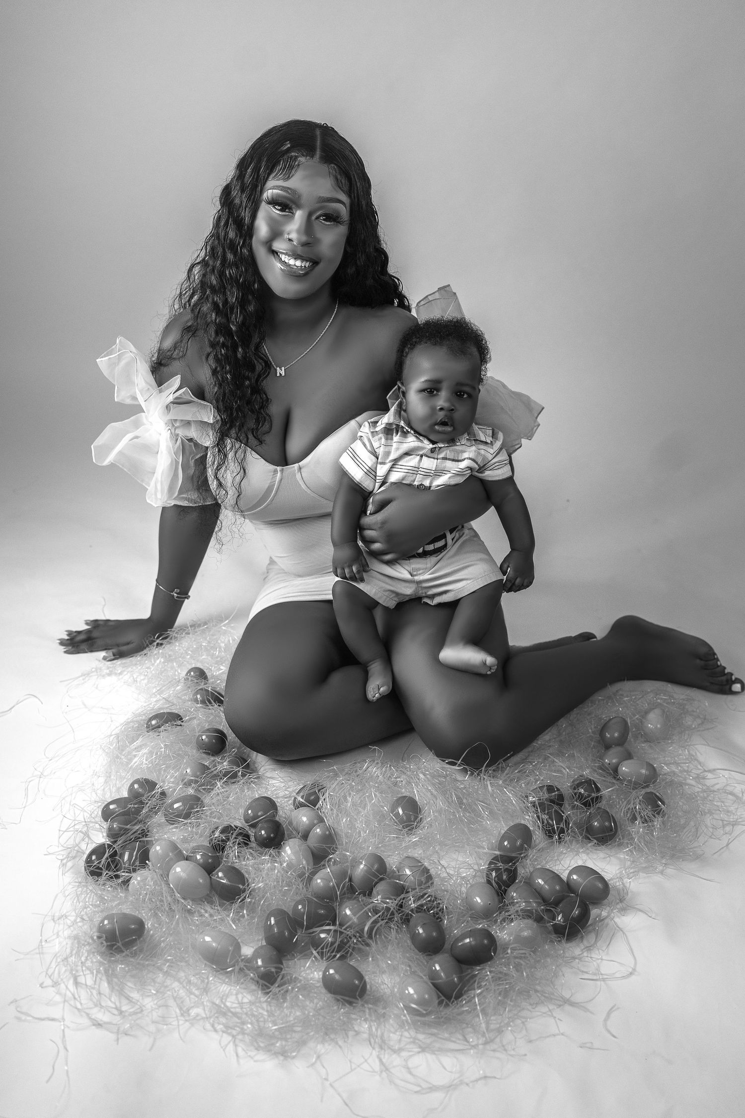 Black and white photo of a smiling woman holding her baby surrounded by Easter eggs on a nest.
