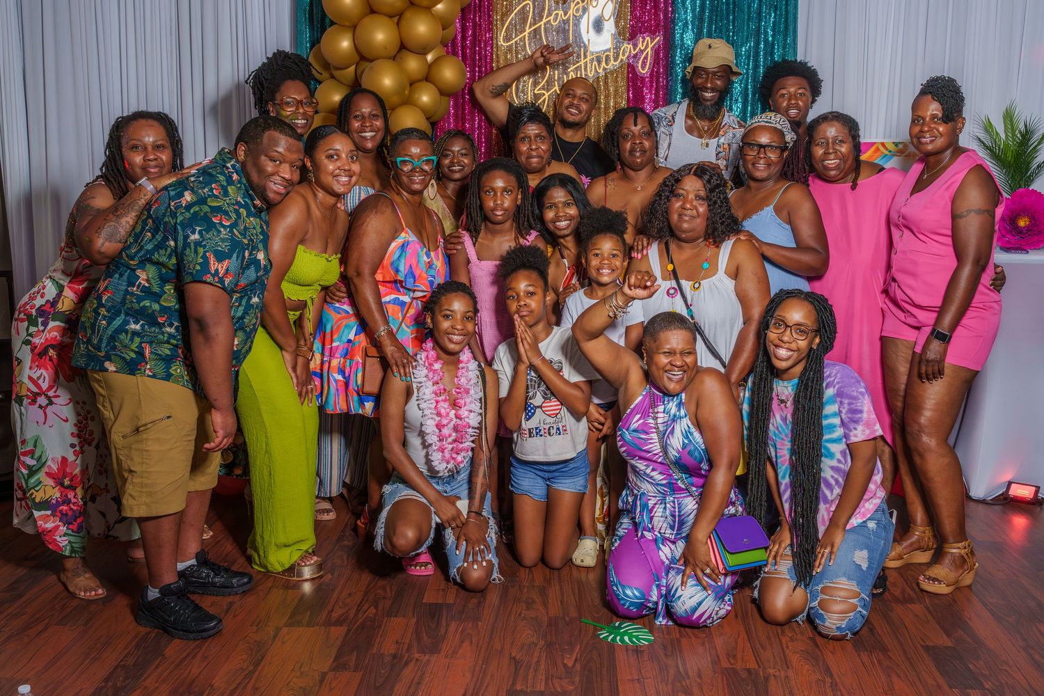 Large group of smiling people posing together at a Happy Birthday celebration indoors.